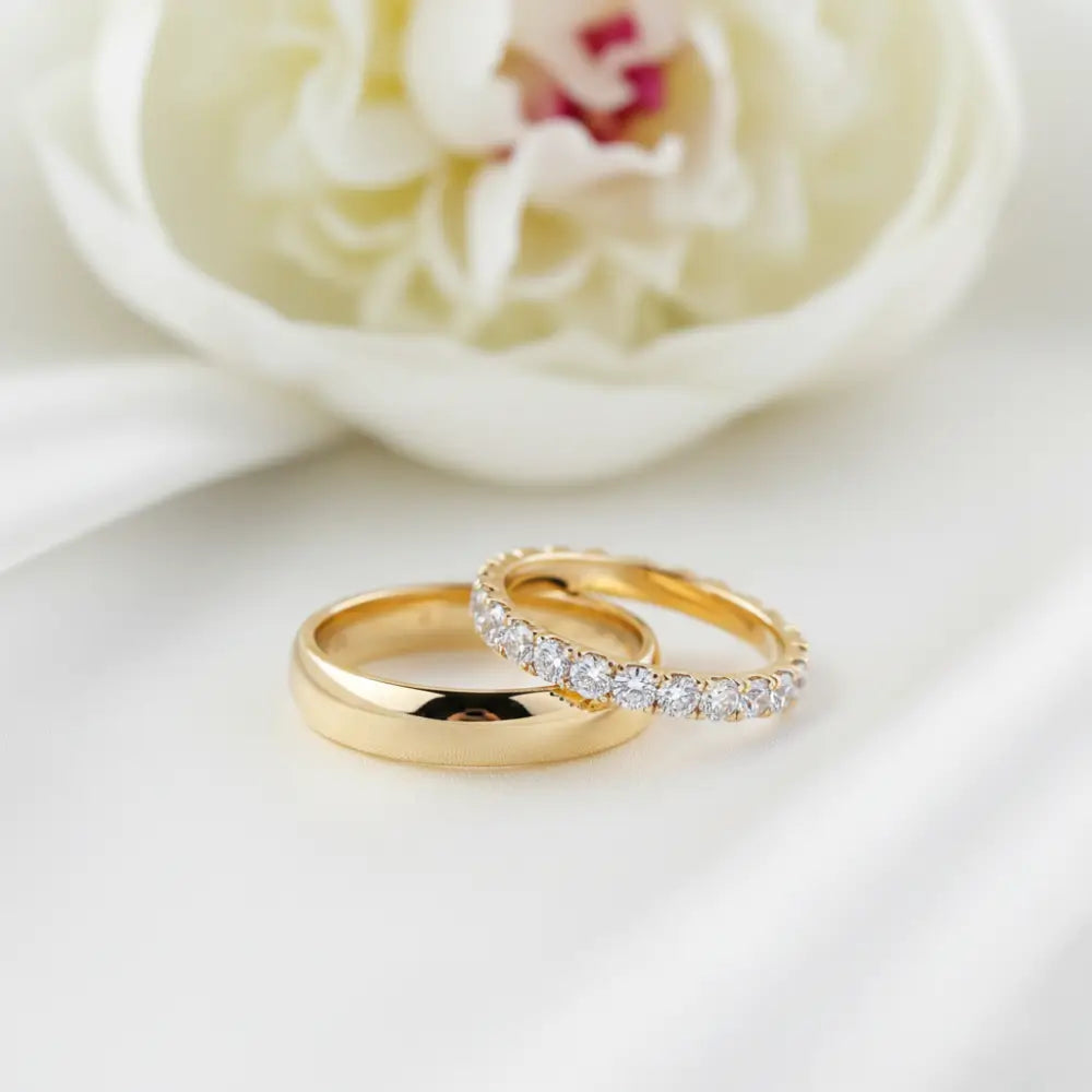 Gold wedding rings on white fabric, flower background, elegant jewelry