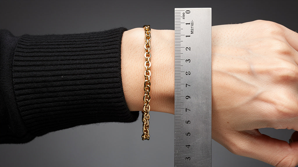 Gold chain bracelet on a woman's wrist with a ruler showing bracelet size