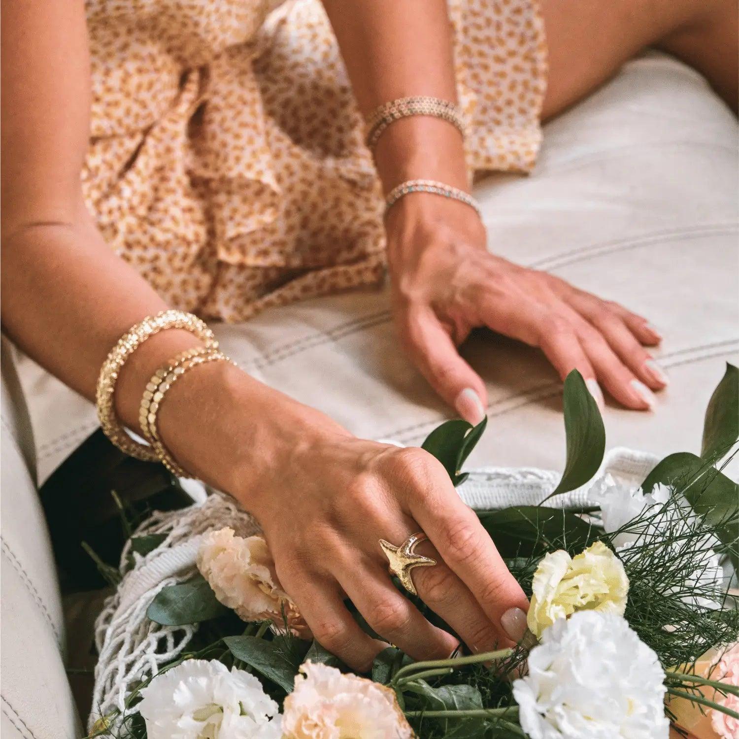 Image featuring a model wearing a stack of Golden Planet's elegant women's 14k gold bracelets and a starfish ring, highlighting summer vacation and effortless luxury.