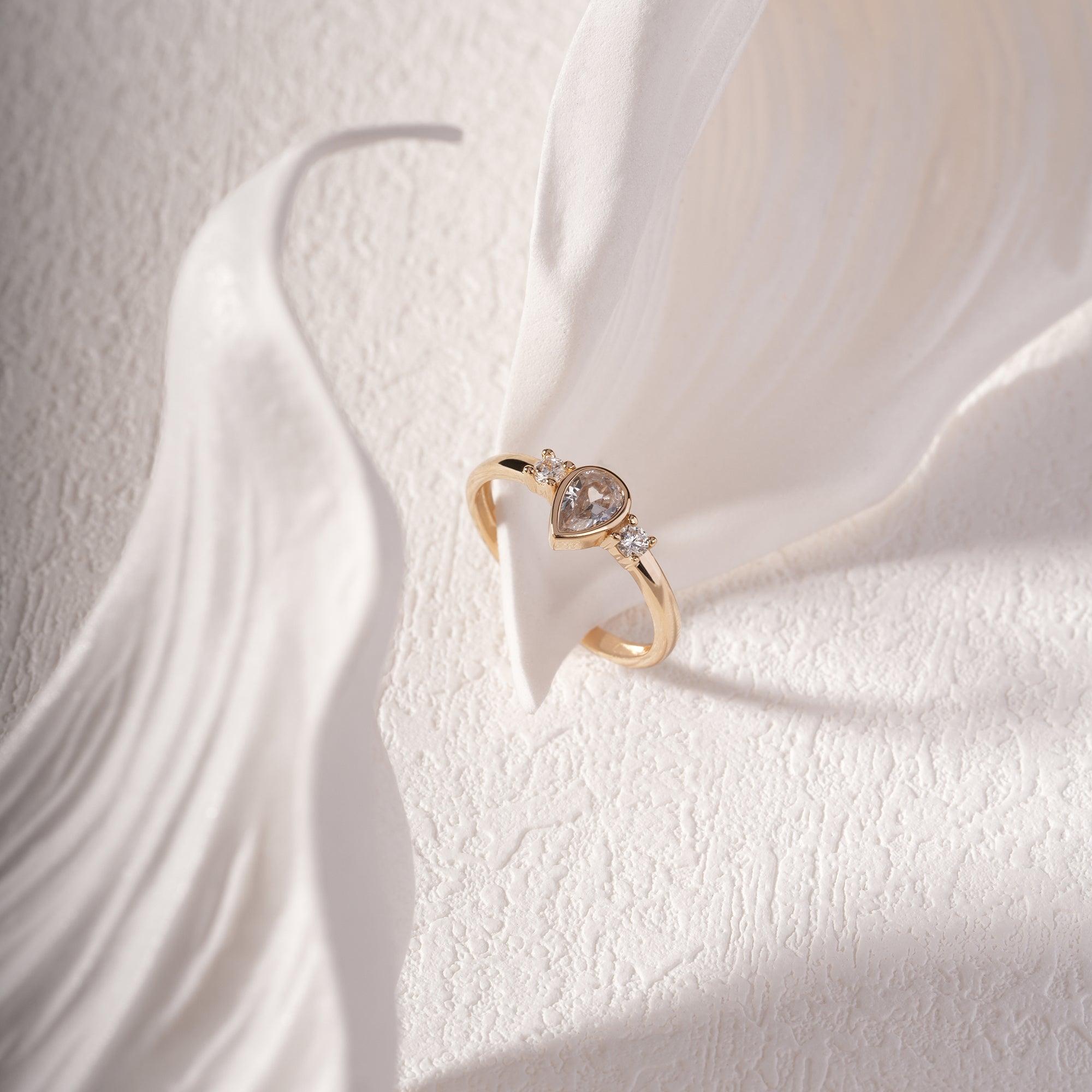 Gold ring with pear-shaped gemstone and accent diamonds on textured white background