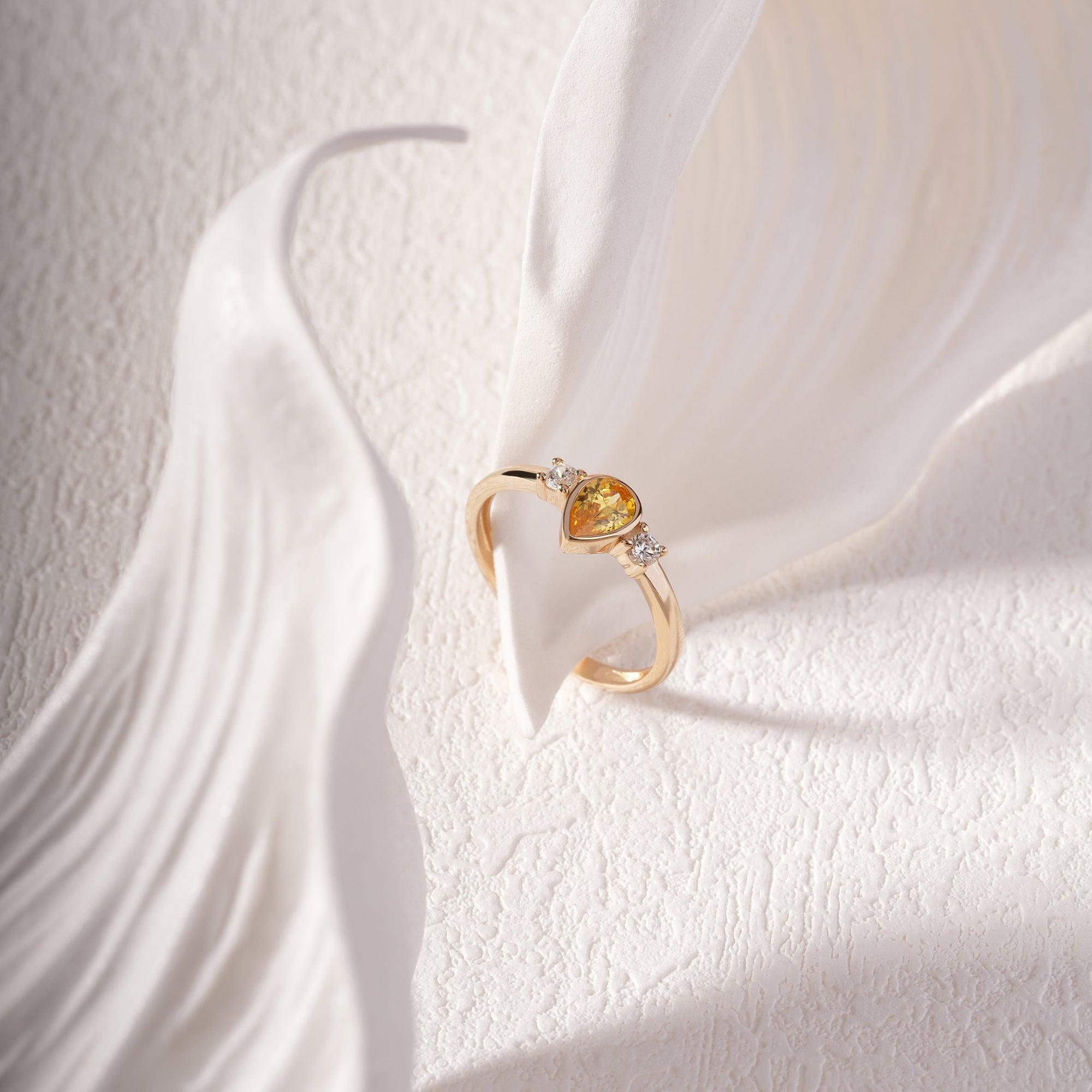 Gold ring with yellow gemstone and diamonds displayed on white textured background