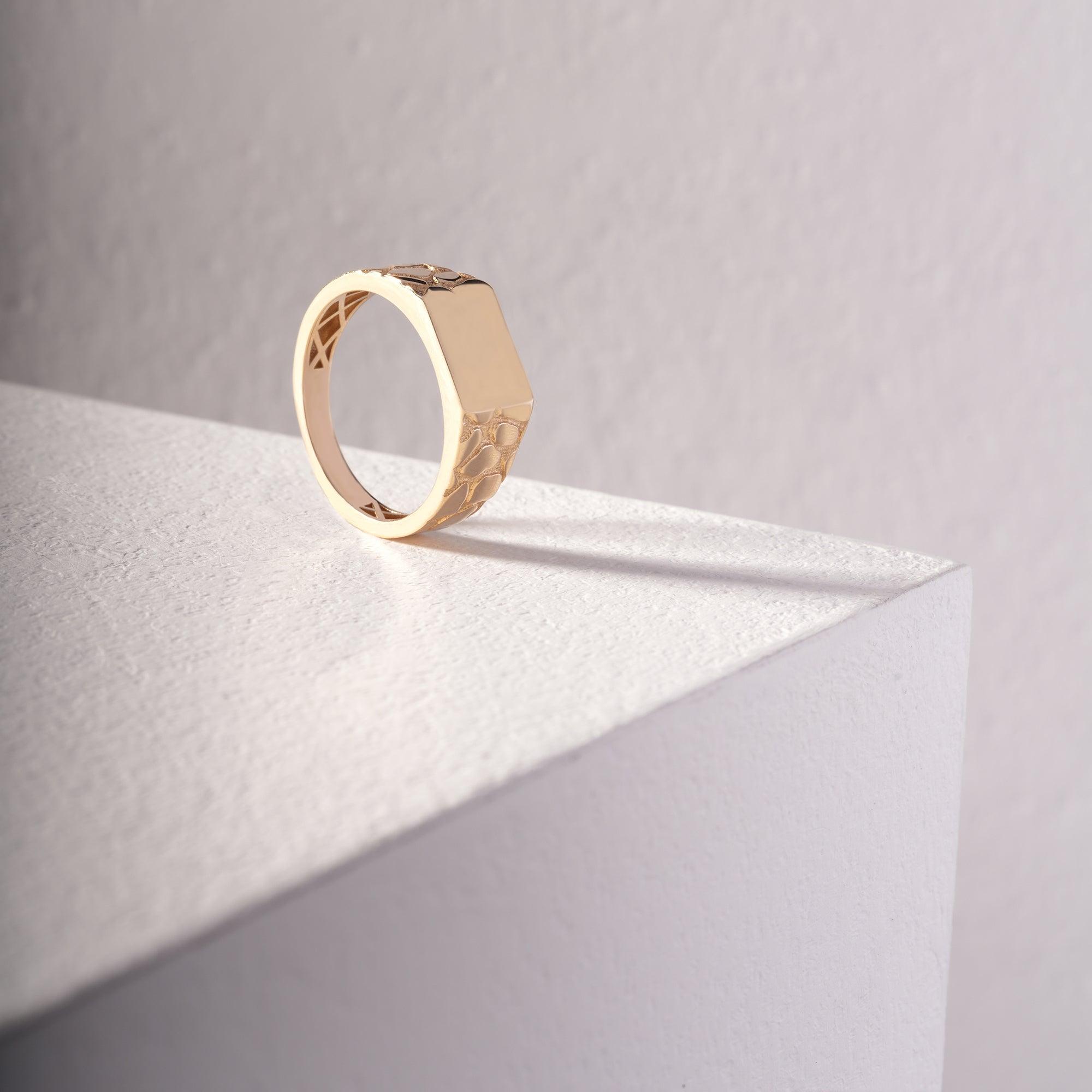 Geometric gold ring with textured pattern on a white minimalist display