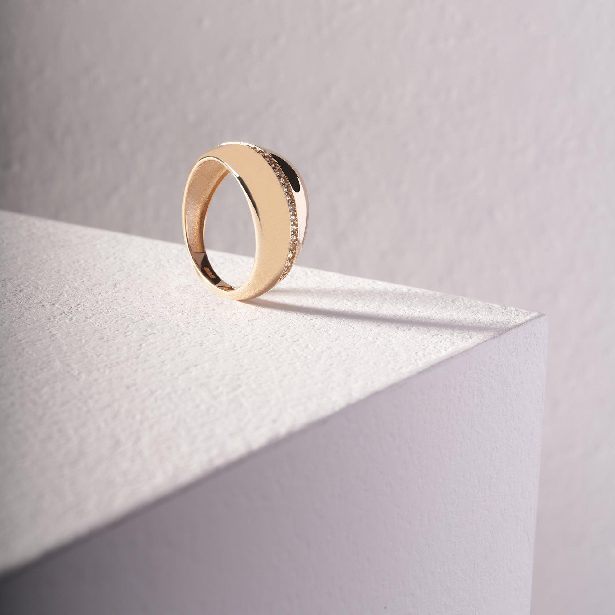 Gold ring with a row of small diamonds on a textured white surface, minimalist background
