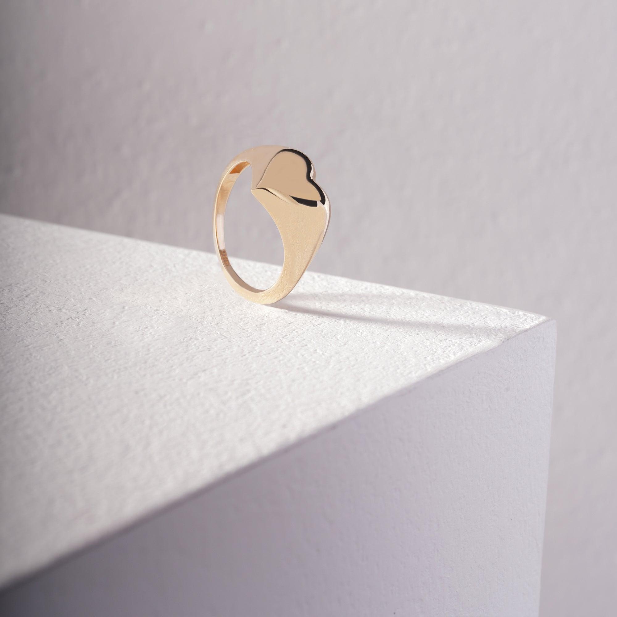 Minimalist gold heart ring displayed on white textured stand