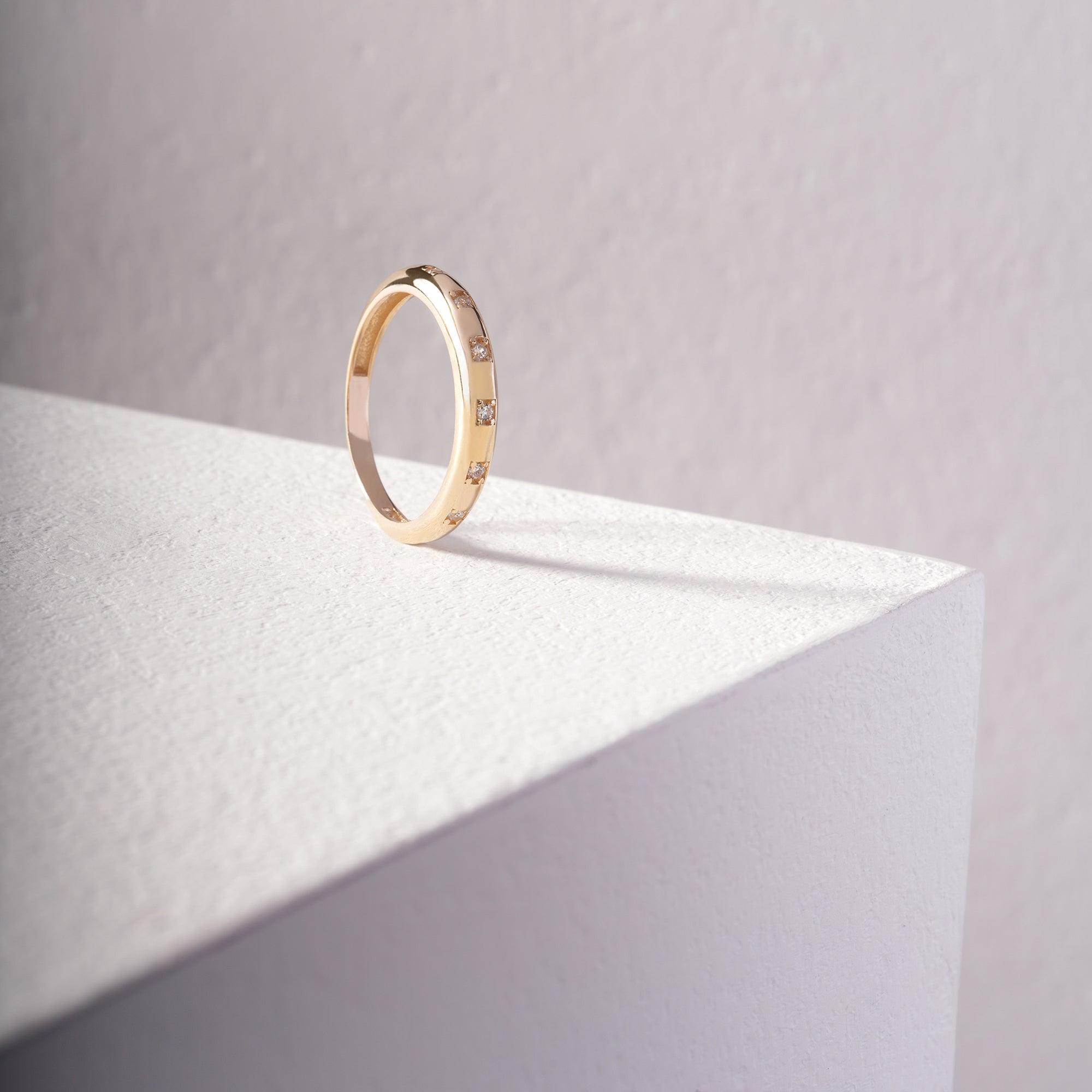 Gold ring with small gemstones on minimalist white pedestal, elegant jewelry product photo