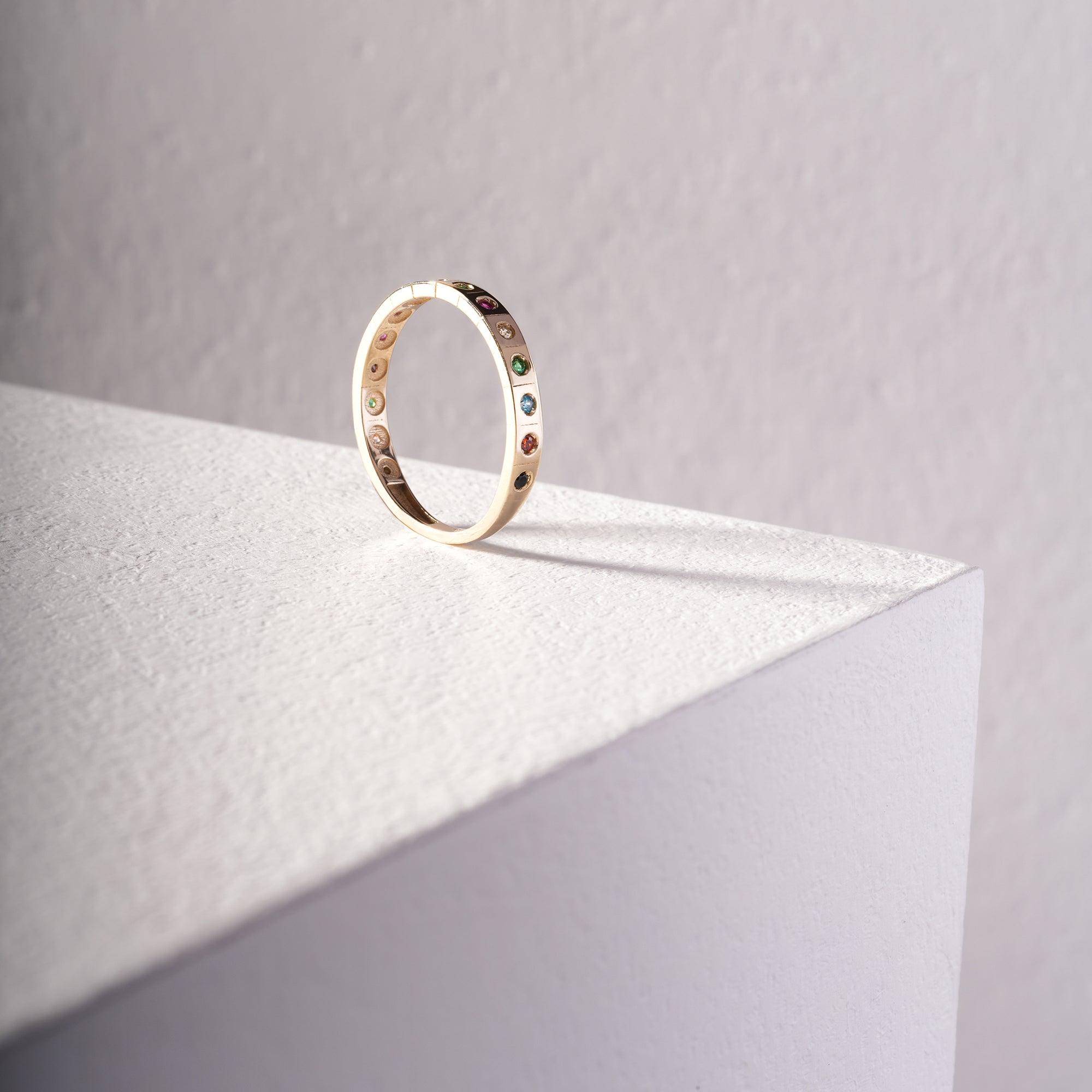Gold ring with colorful gemstones displayed on a white textured surface, minimalist setting