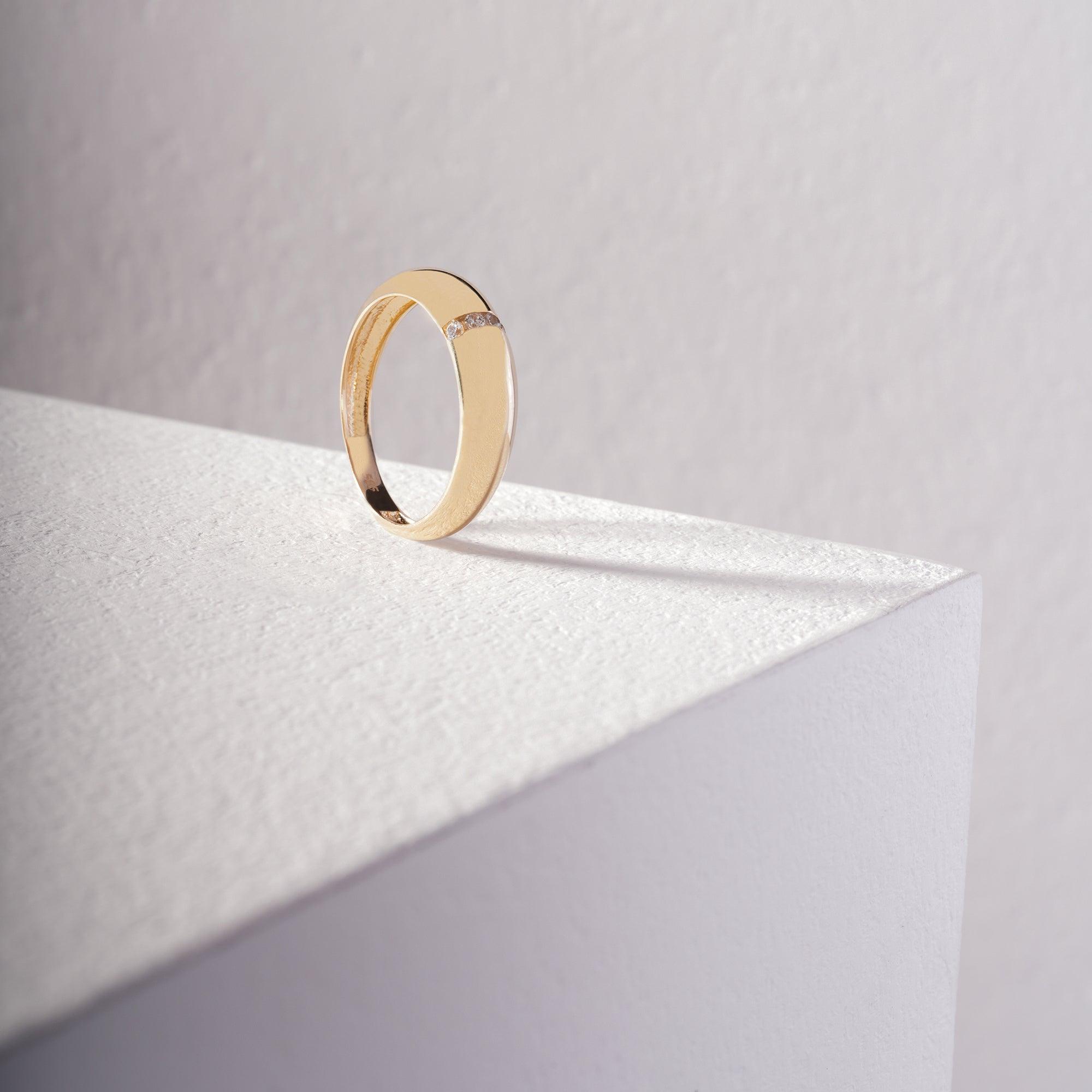 Gold ring with diamond accents on a textured white surface, minimalist jewelry design