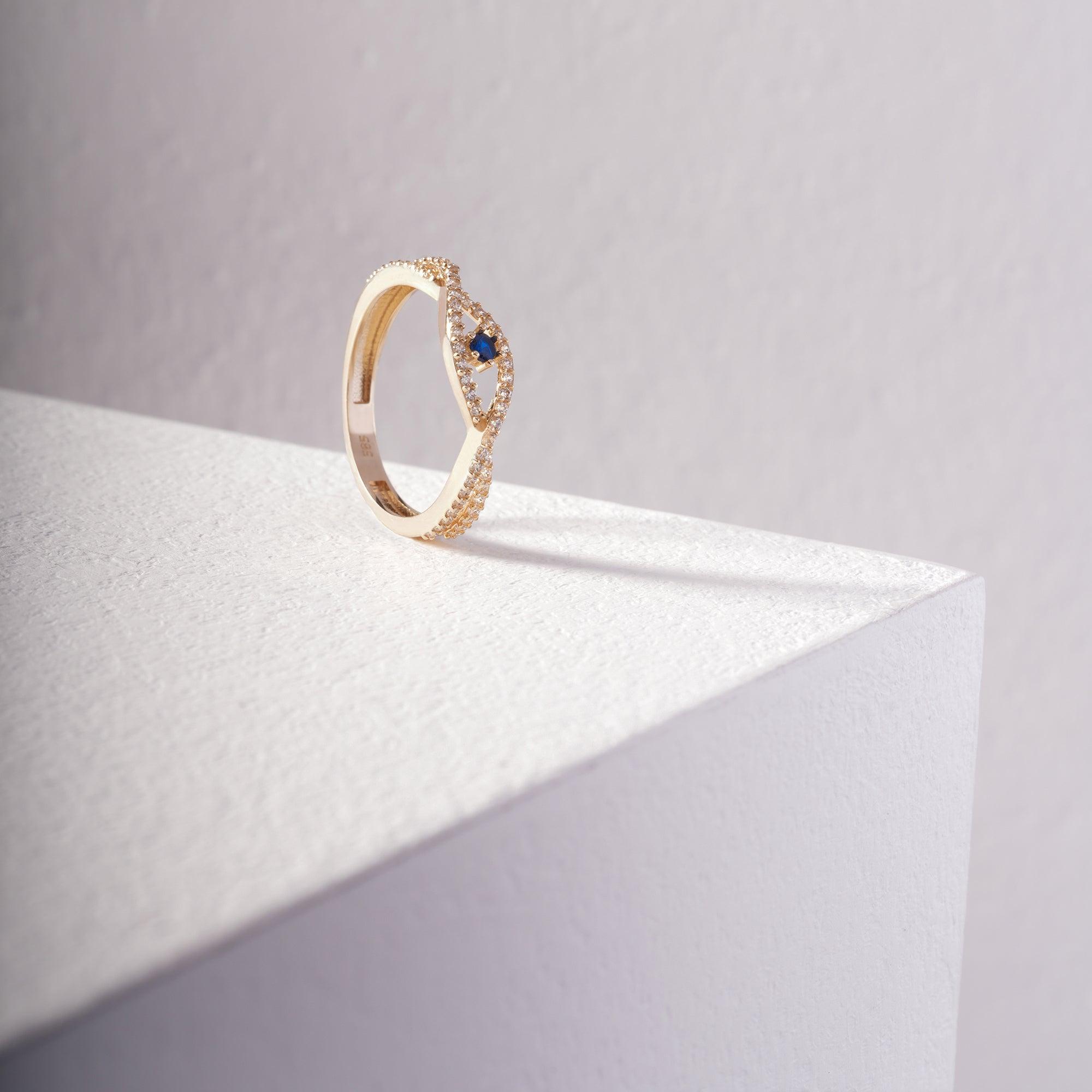 Gold ring with blue gemstone and diamond accents on a minimalist white pedestal