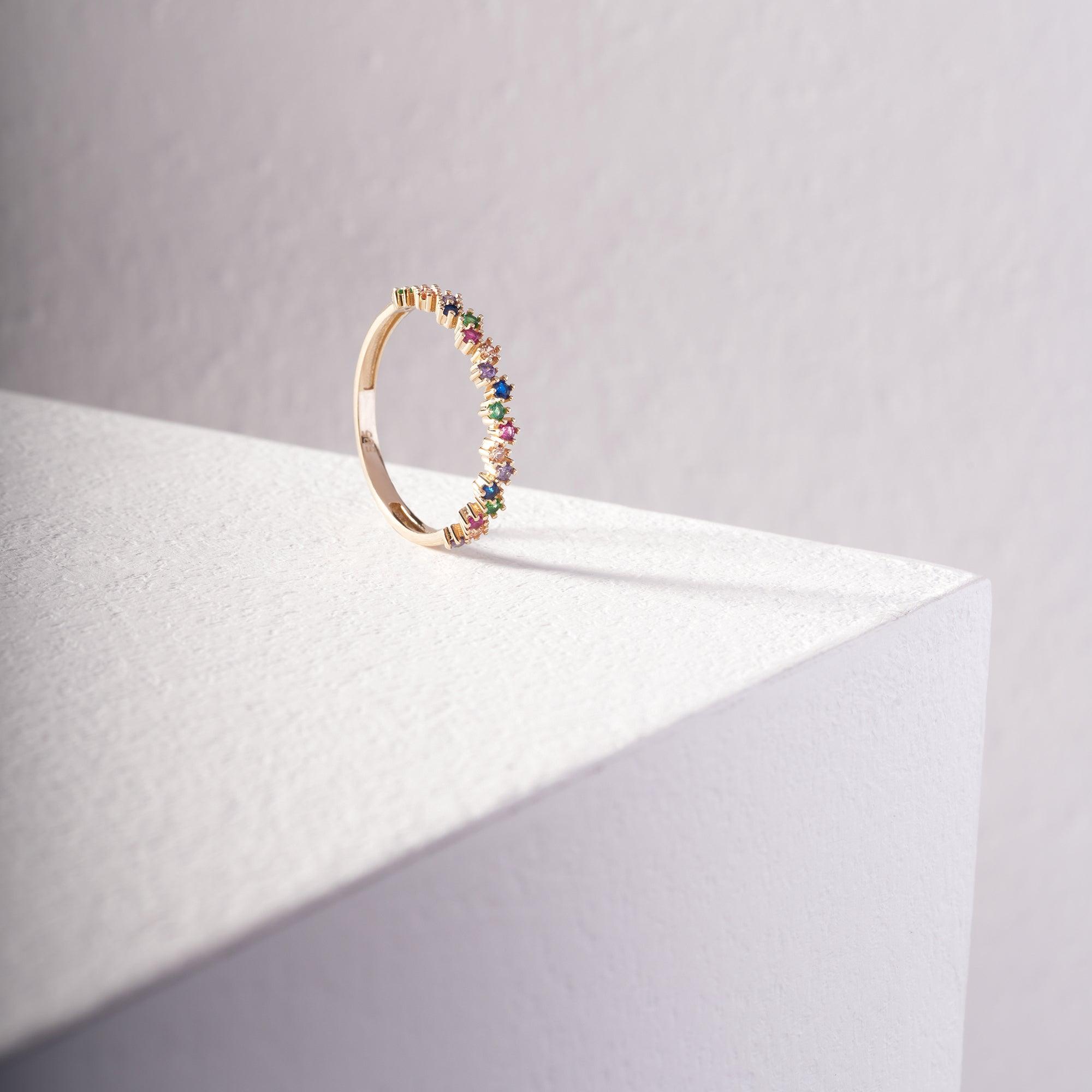 Gold ring with colorful gemstones displayed on a white textured surface