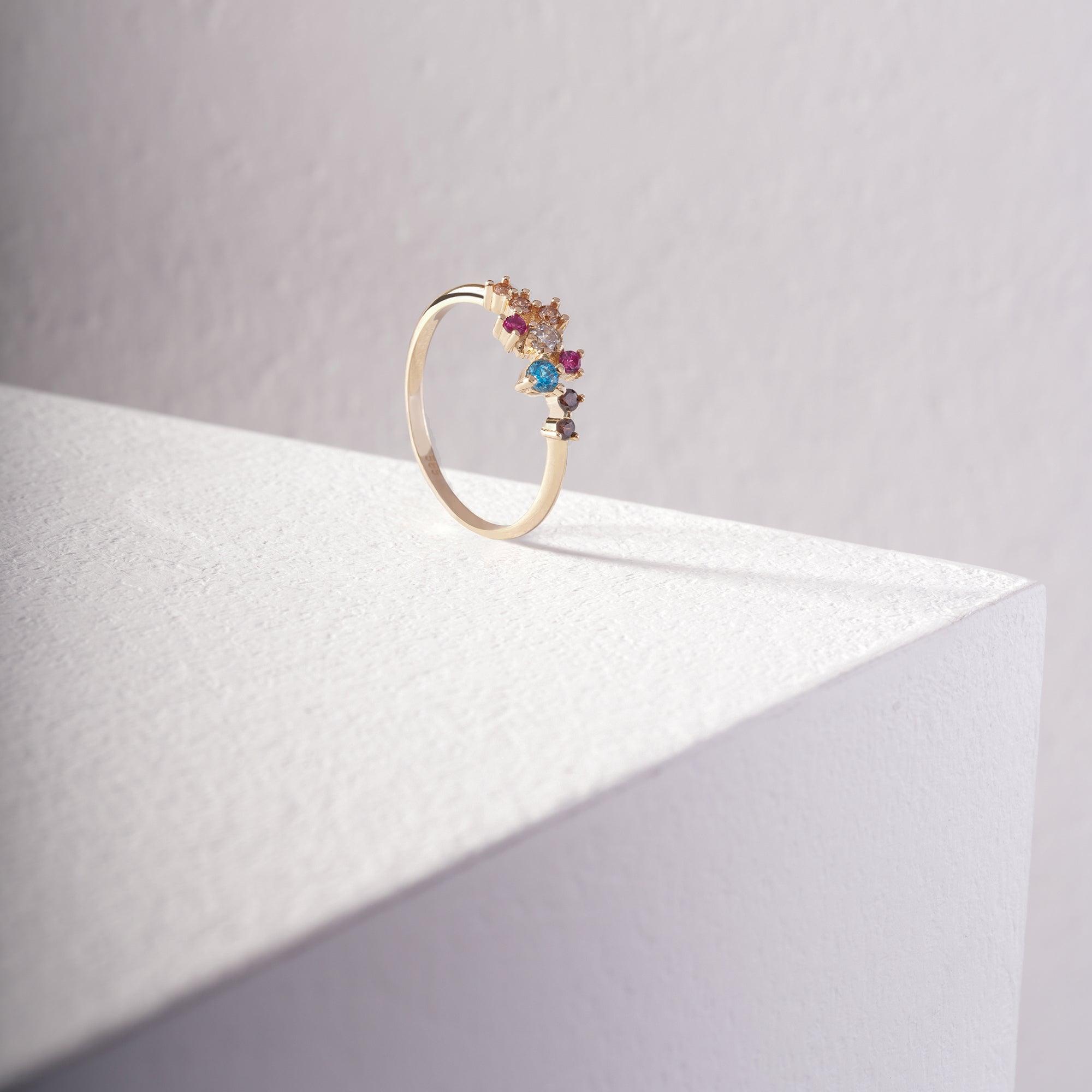 Gold ring with colorful gemstones displayed on a white textured surface