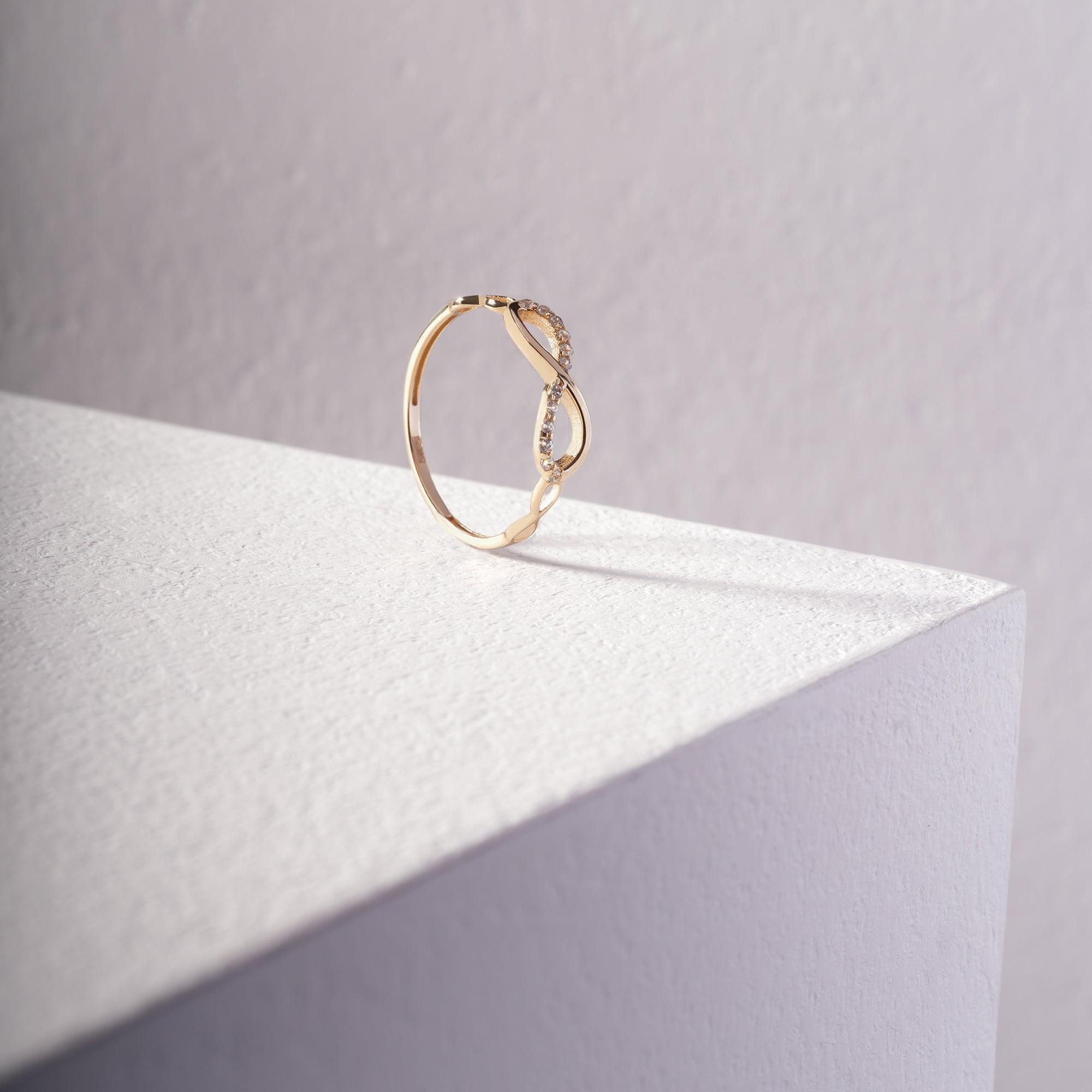Delicate gold ring with curved band and small gemstones on minimal white surface