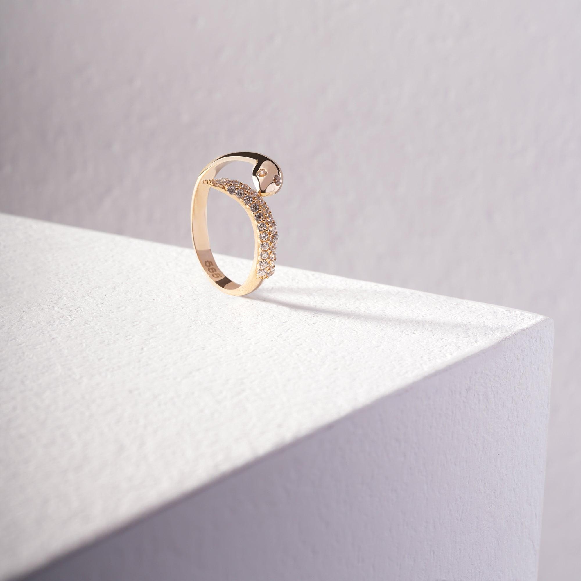 Gold ring with pavé-set stones on white textured surface, minimalist jewelry design.