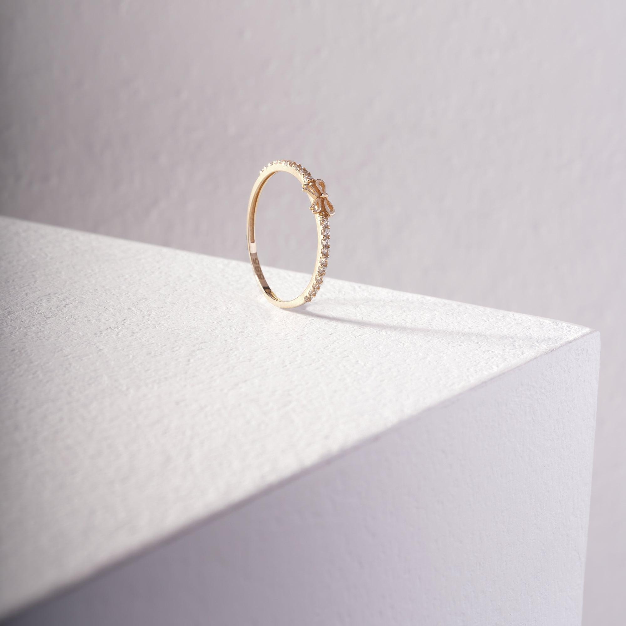 Delicate gold ring with small bow and pavé diamonds on a white textured surface