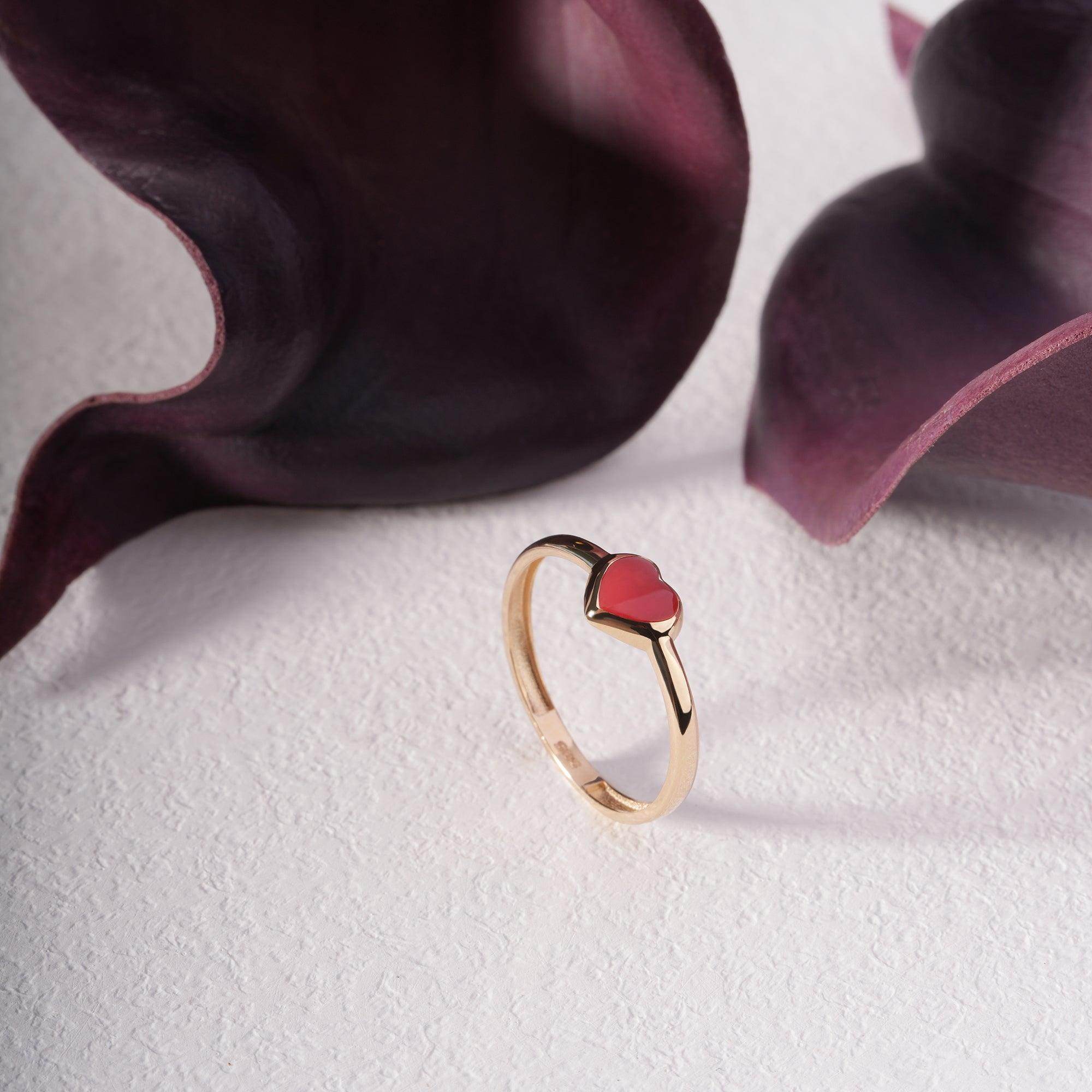 Gold ring with red heart-shaped gemstone on textured white surface and purple floral accents
