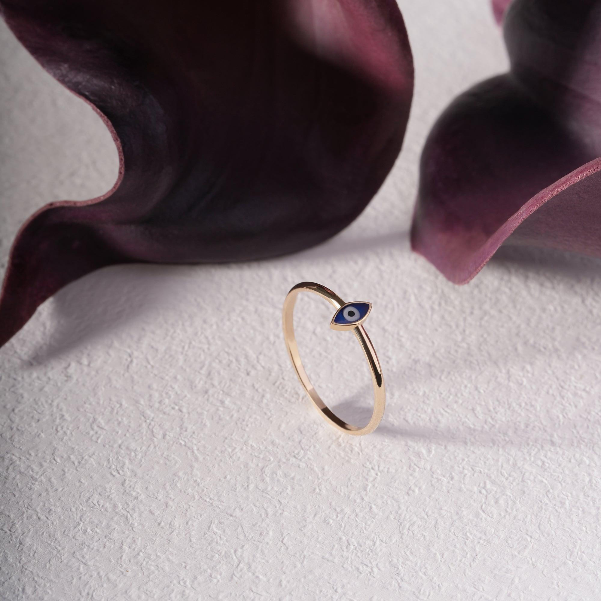 Minimalist gold ring with blue evil eye charm on textured white surface, purple accents
