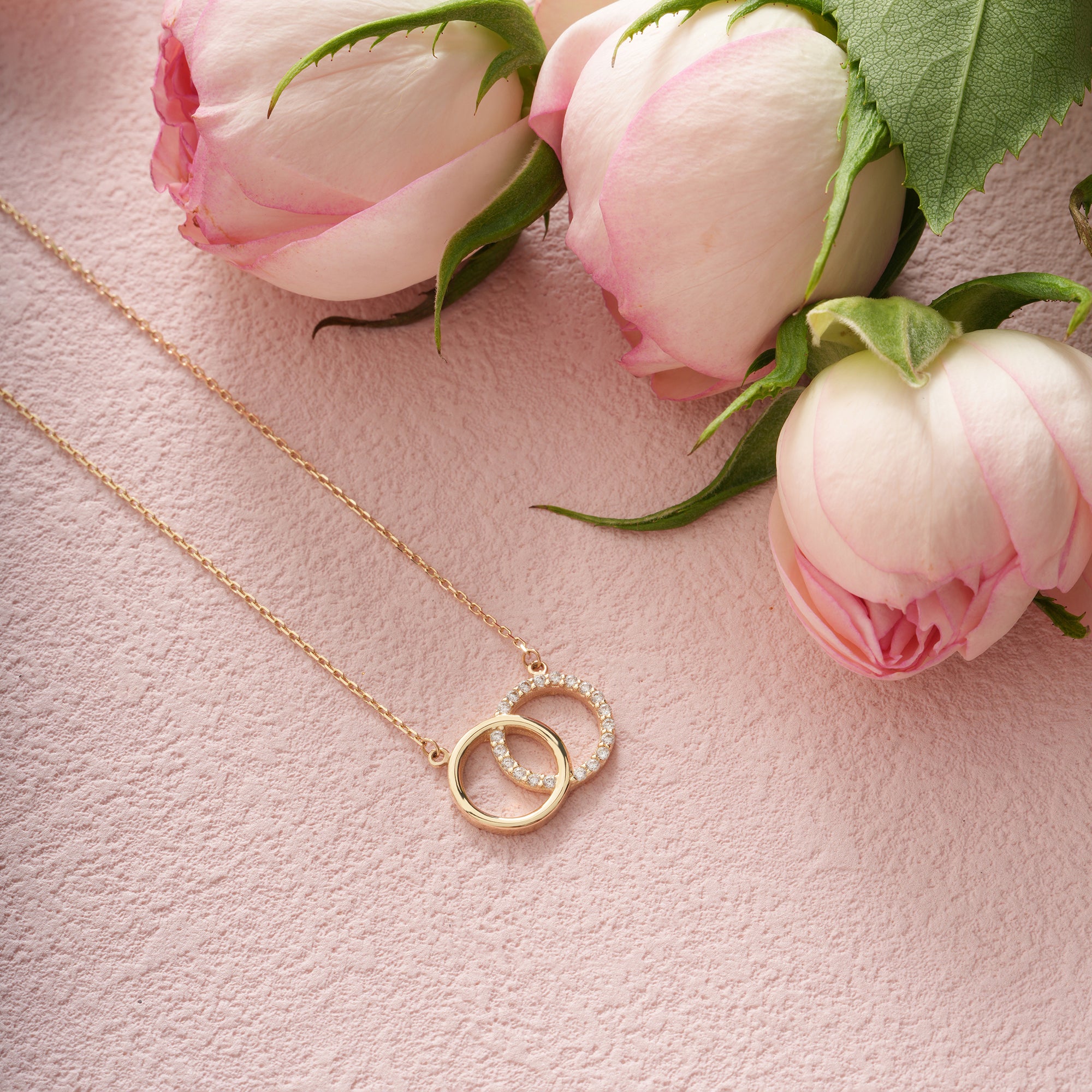 Gold necklace with interlocking rings on a pink surface with pink roses