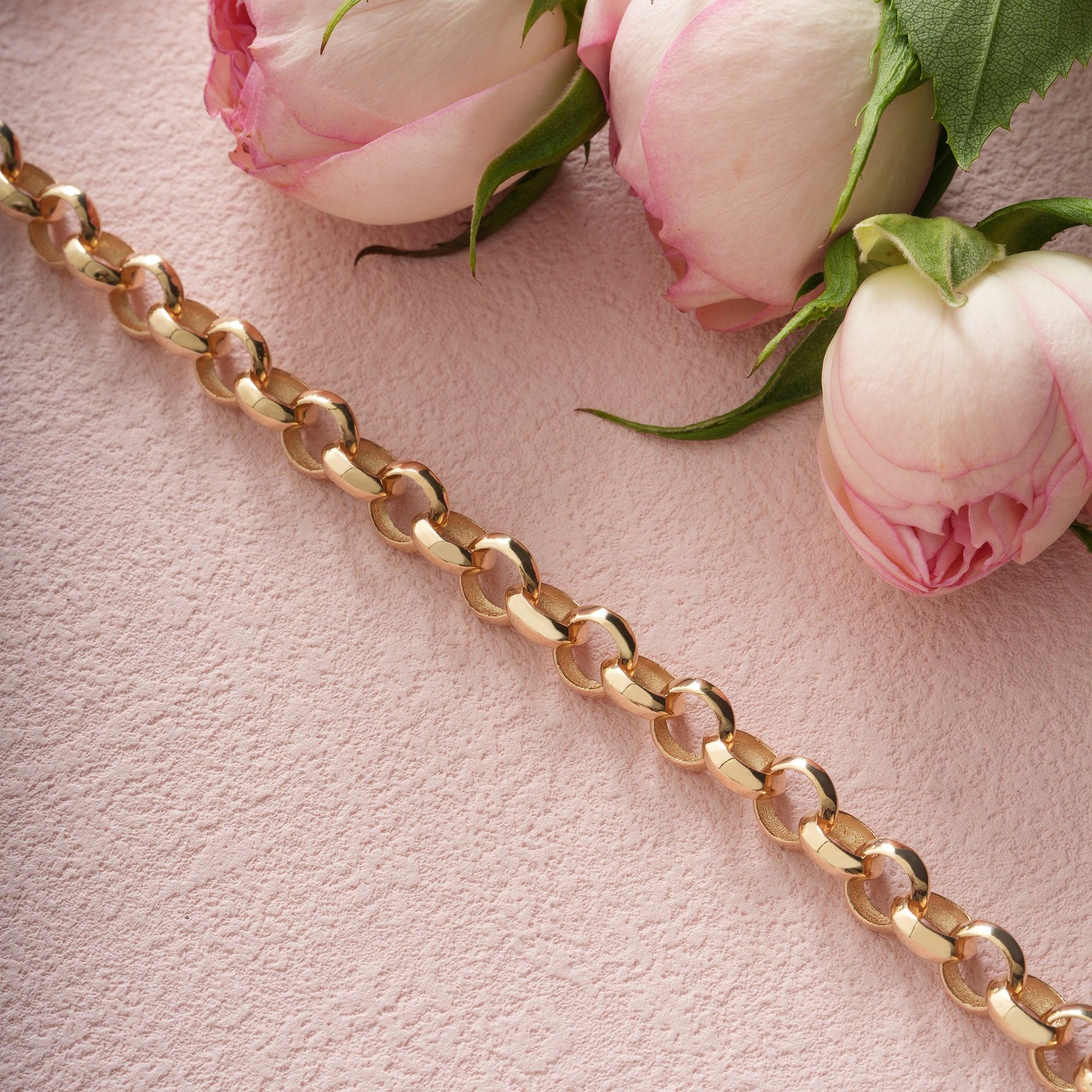 Gold chain bracelet on pink textured background with pink rose flowers