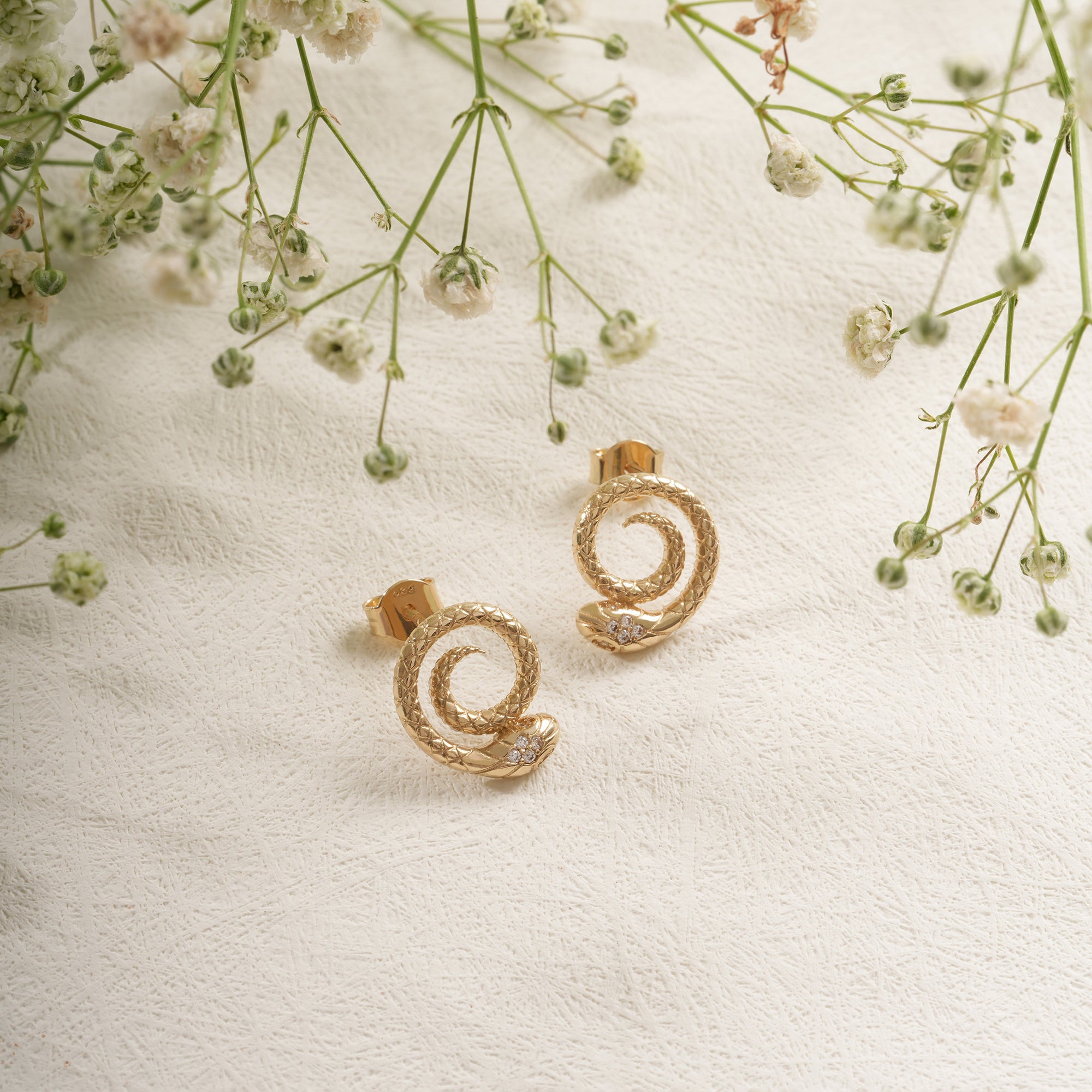 Gold spiral earrings on a textured white surface with delicate flowers.