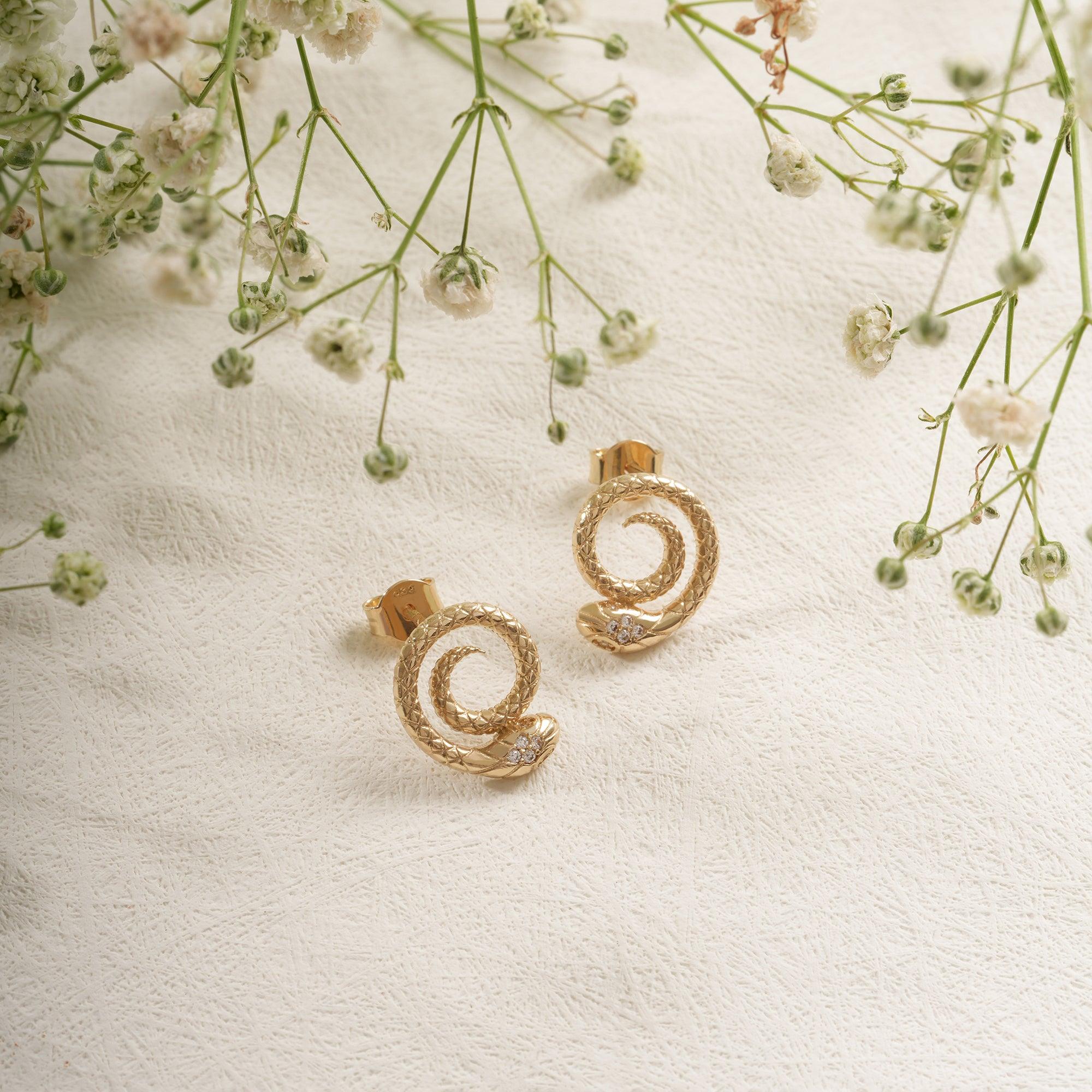 Textured gold spiral earrings with small diamond accents on a white surface, surrounded by delicate flowers.