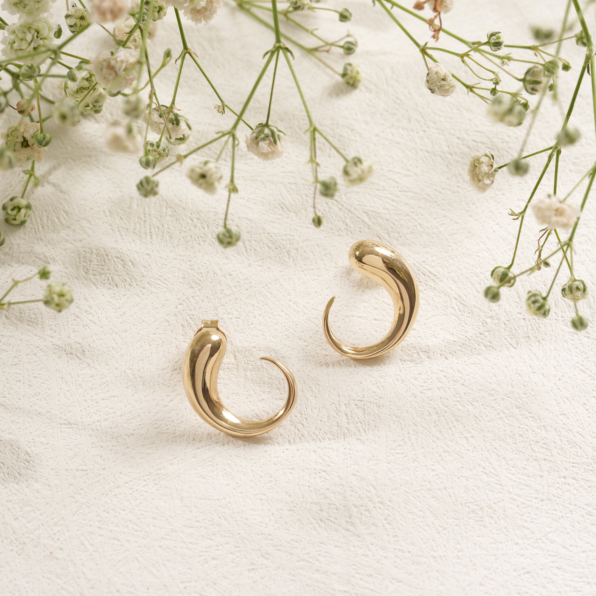 Gold hoop earrings on a white fabric background with small flowers.