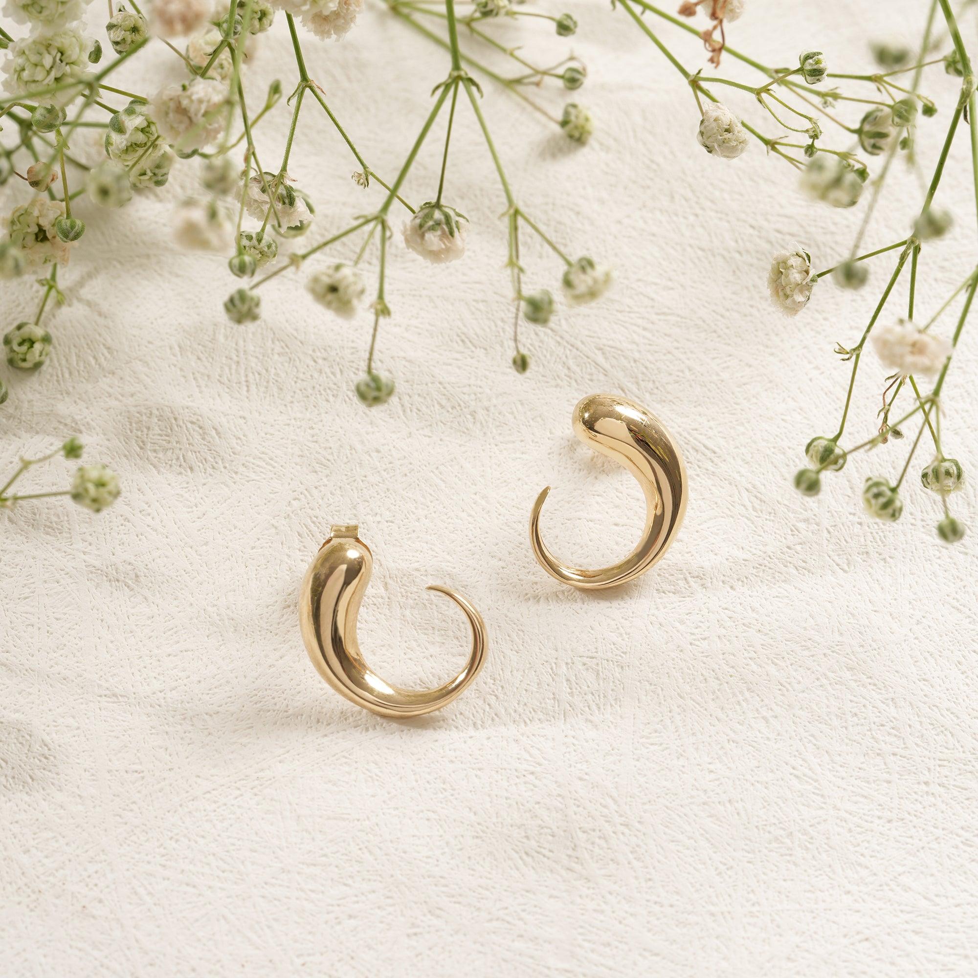 Curved gold hoop earrings on textured fabric with delicate white flowers