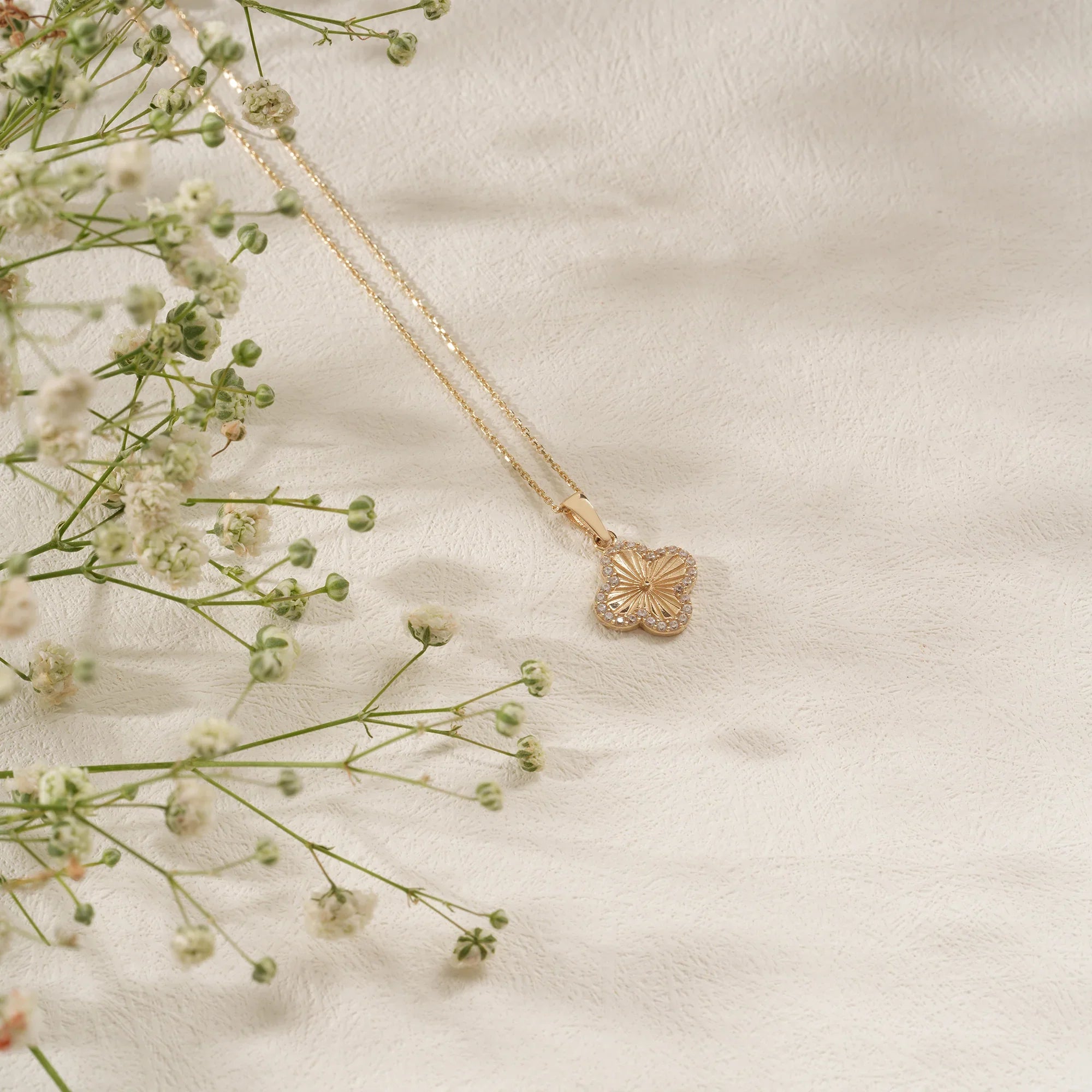 Gold necklace with a floral pendant on a light fabric background