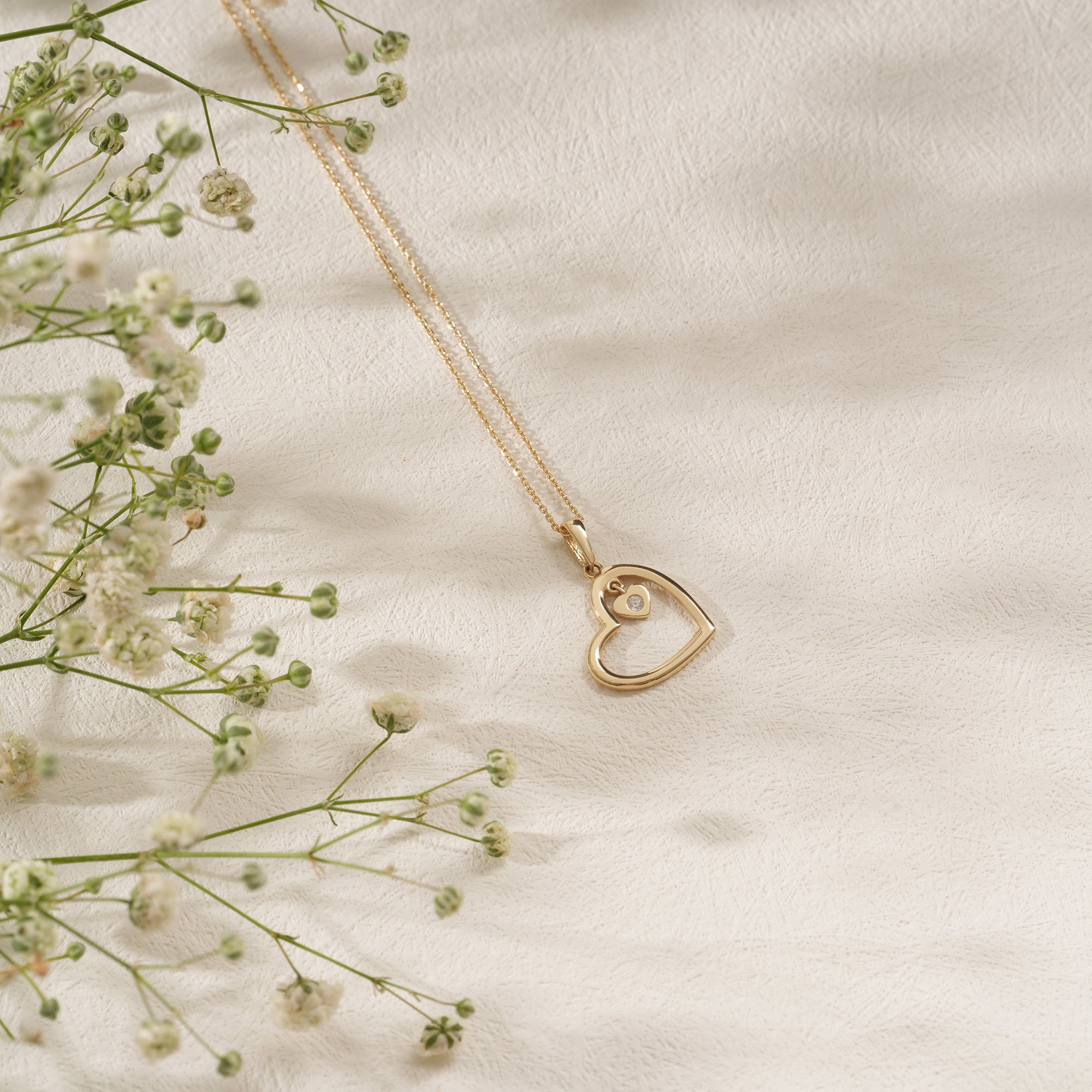 Gold heart-shaped necklace on a soft beige background with delicate flowers.