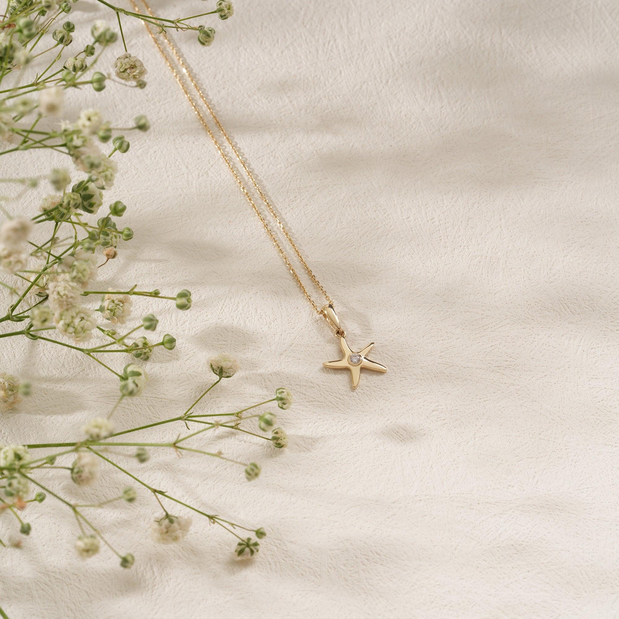 Gold starfish pendant necklace with diamond accent on textured white surface, floral decor