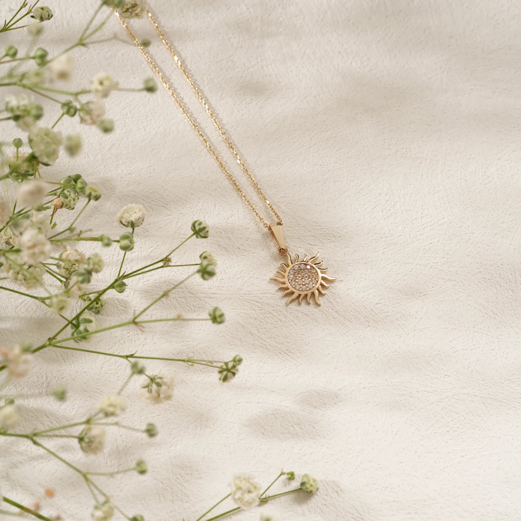 Gold necklace with a sun pendant on a light fabric background