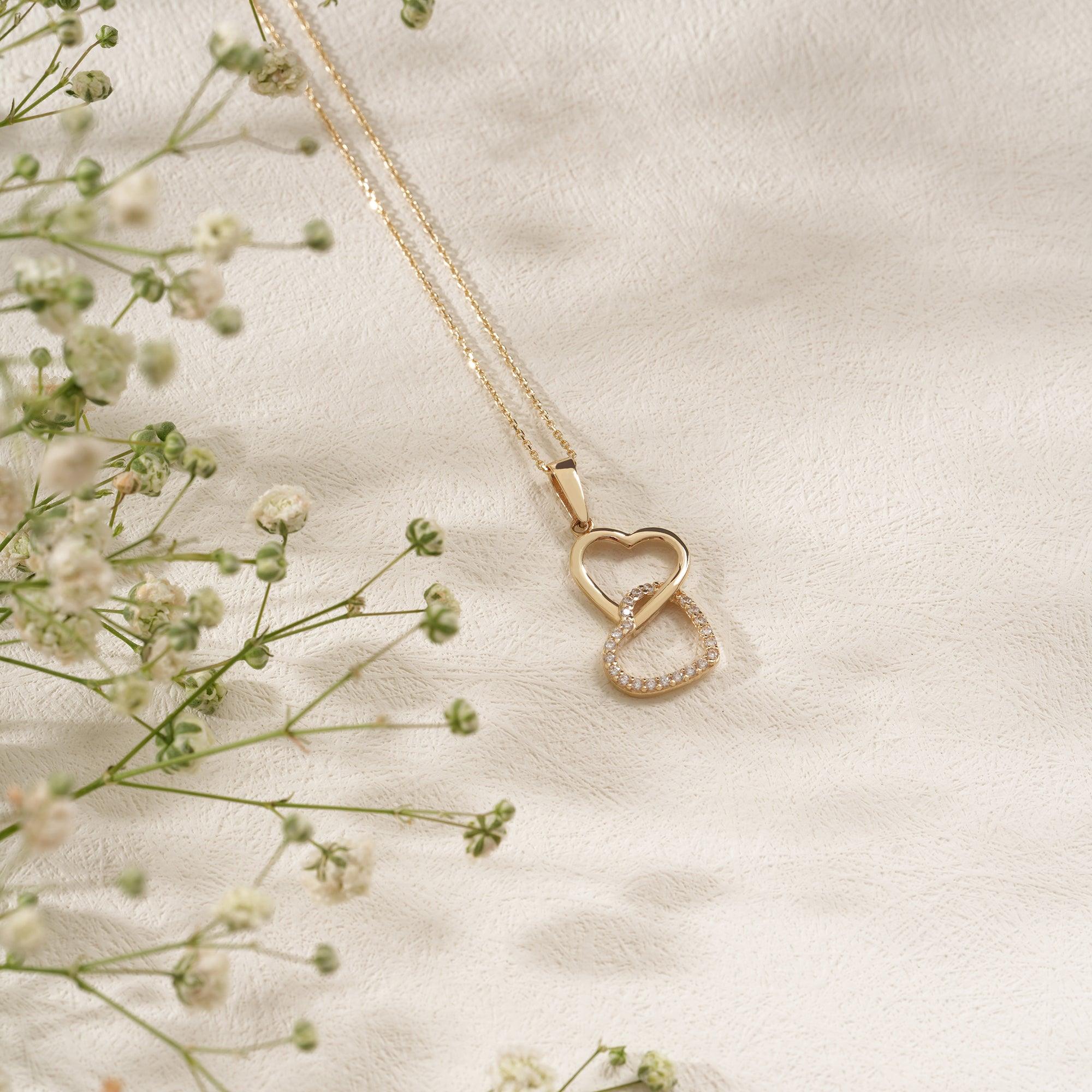 Gold heart and infinity pendant necklace with diamond accents on textured background and flowers