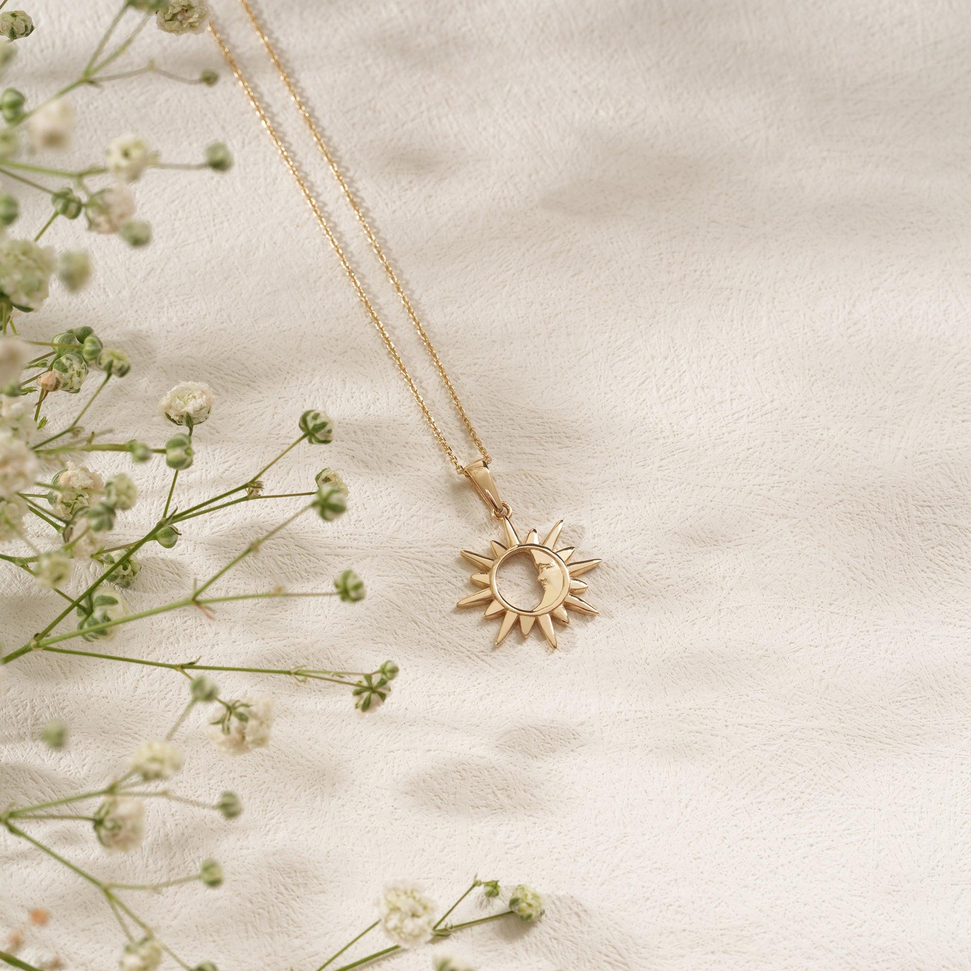 Gold sun and moon pendant necklace on textured fabric with delicate white flowers