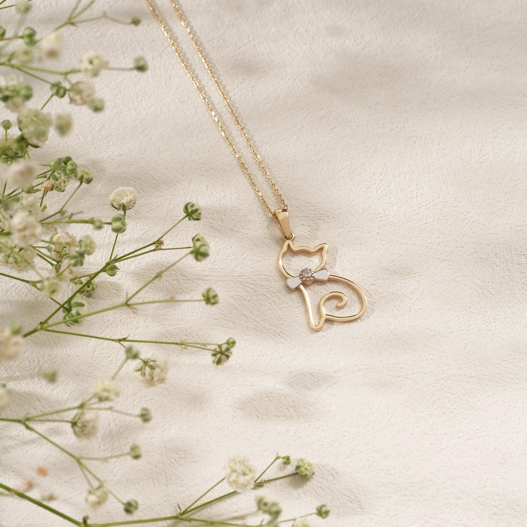 Gold cat pendant necklace with flower detail on textured cream background, with baby's breath flowers.
