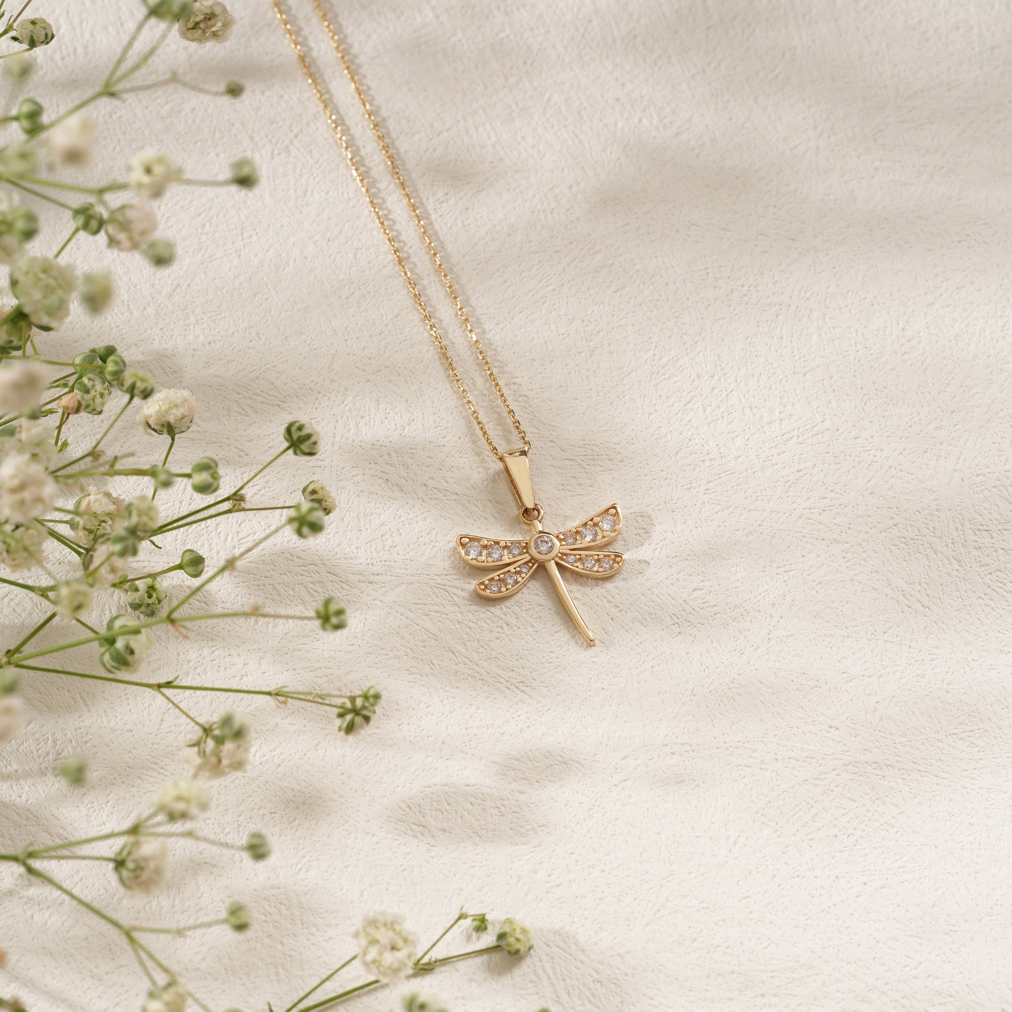 Gold necklace with a dragonfly pendant on a soft beige background with delicate flowers.