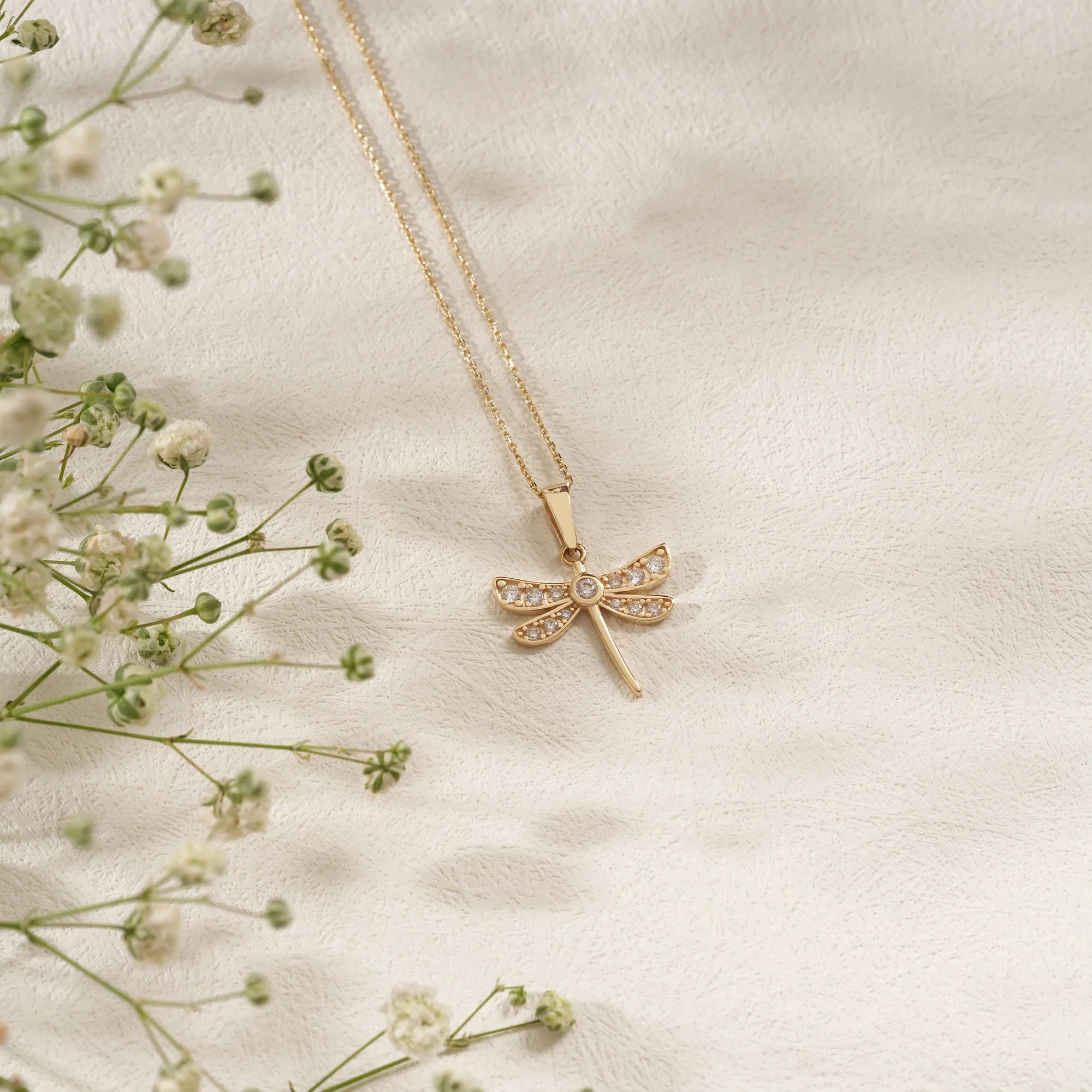 Gold necklace with a dragonfly pendant on a soft beige background with delicate flowers.