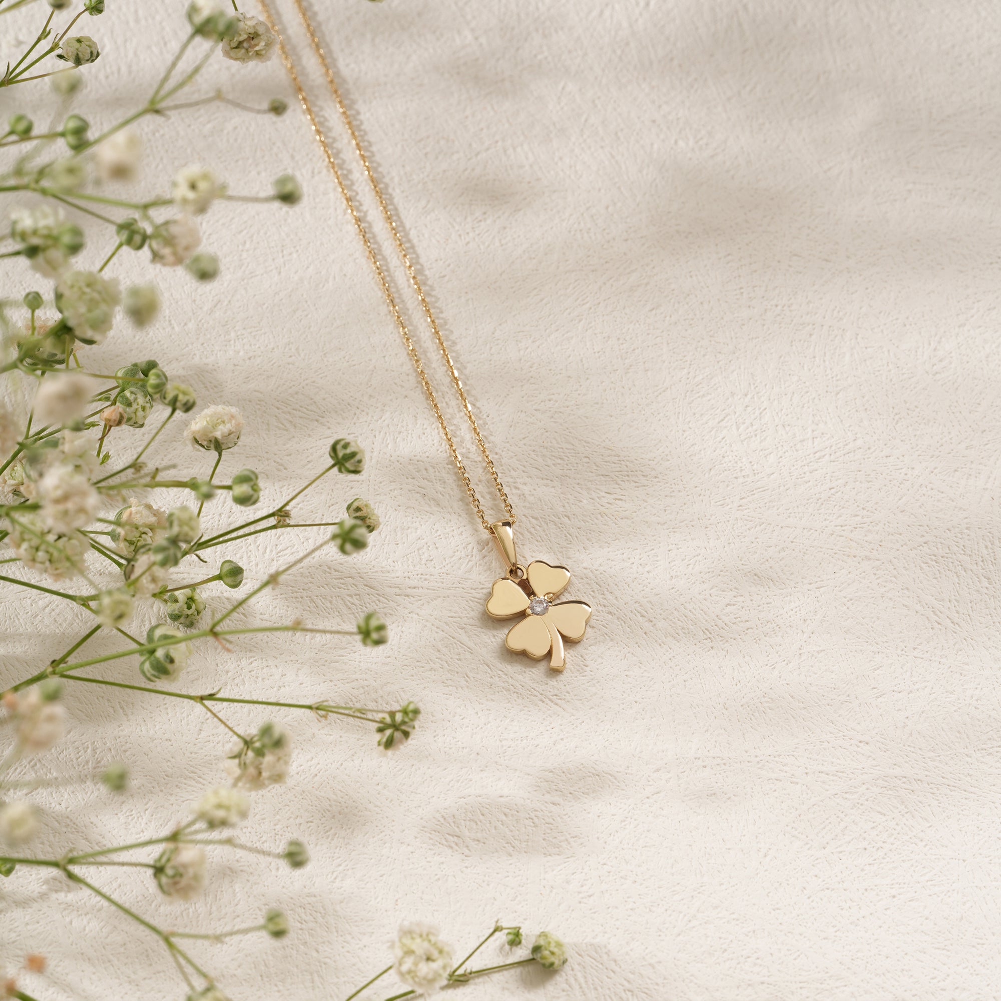 Gold four-leaf clover necklace on a light fabric background with small flowers.