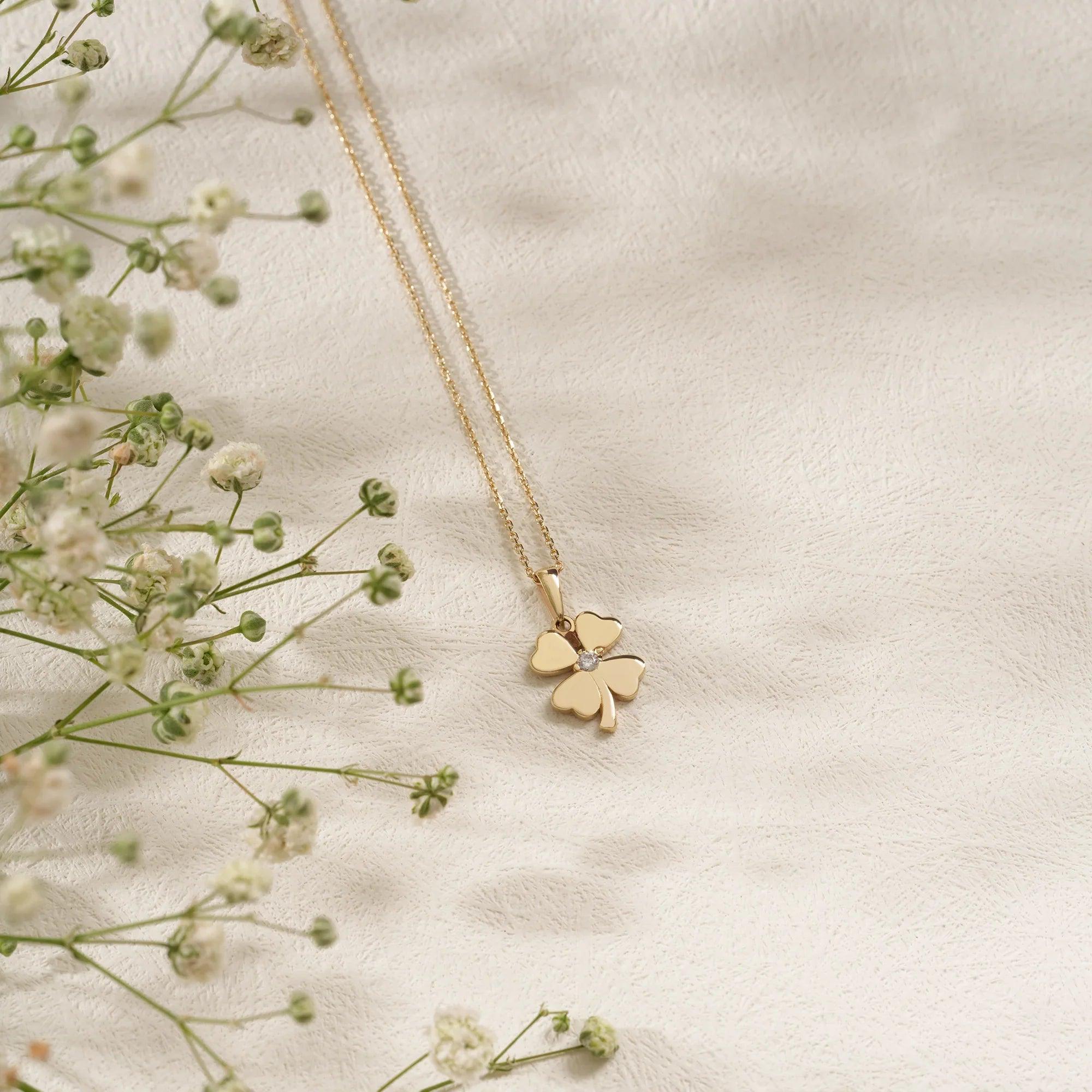 Gold four-leaf clover pendant necklace with diamond accent on textured white background