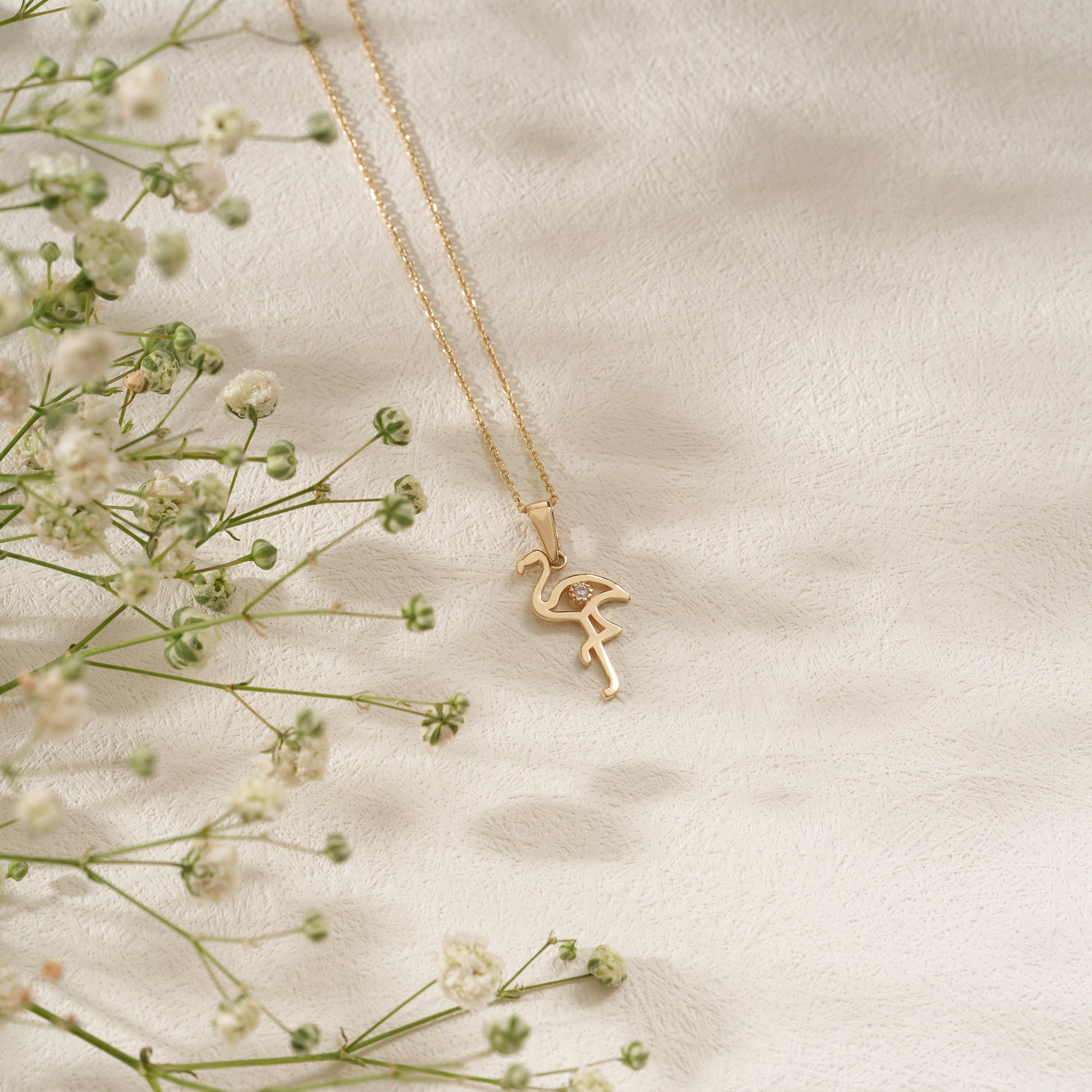 Gold flamingo pendant necklace on a light background with delicate flowers