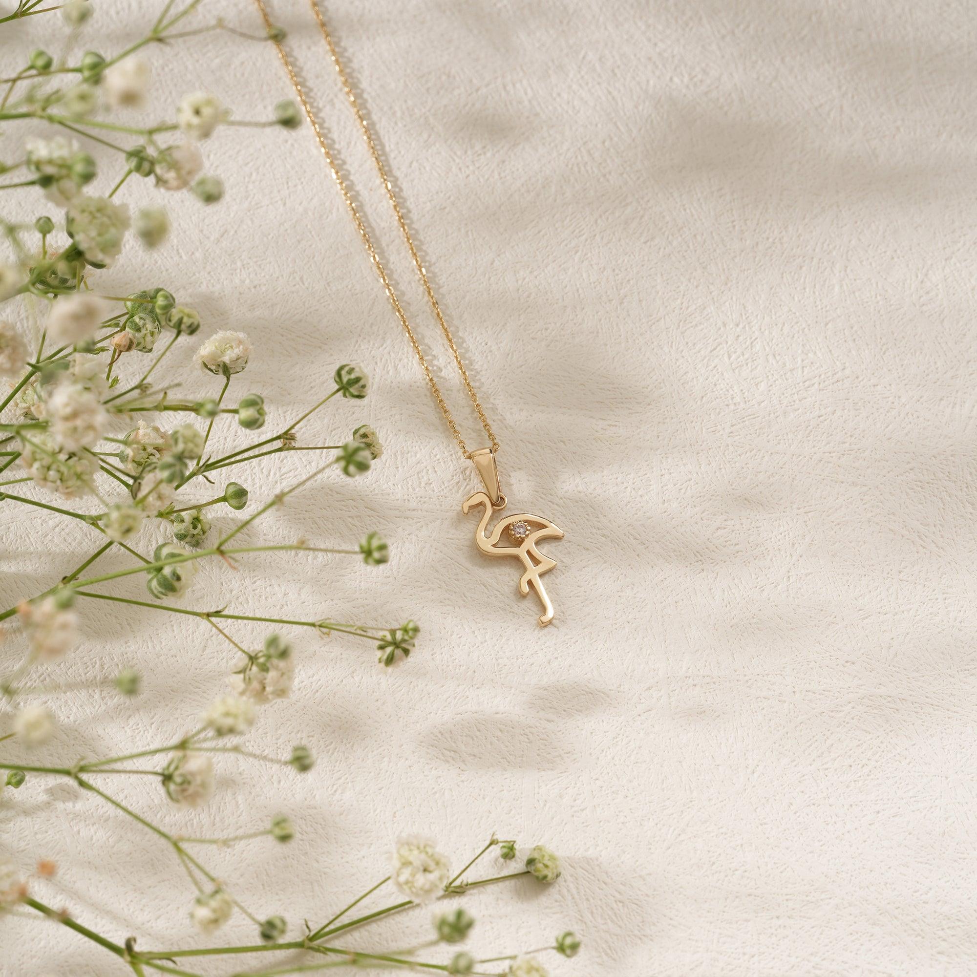 Gold flamingo pendant necklace on soft fabric with delicate white flowers
