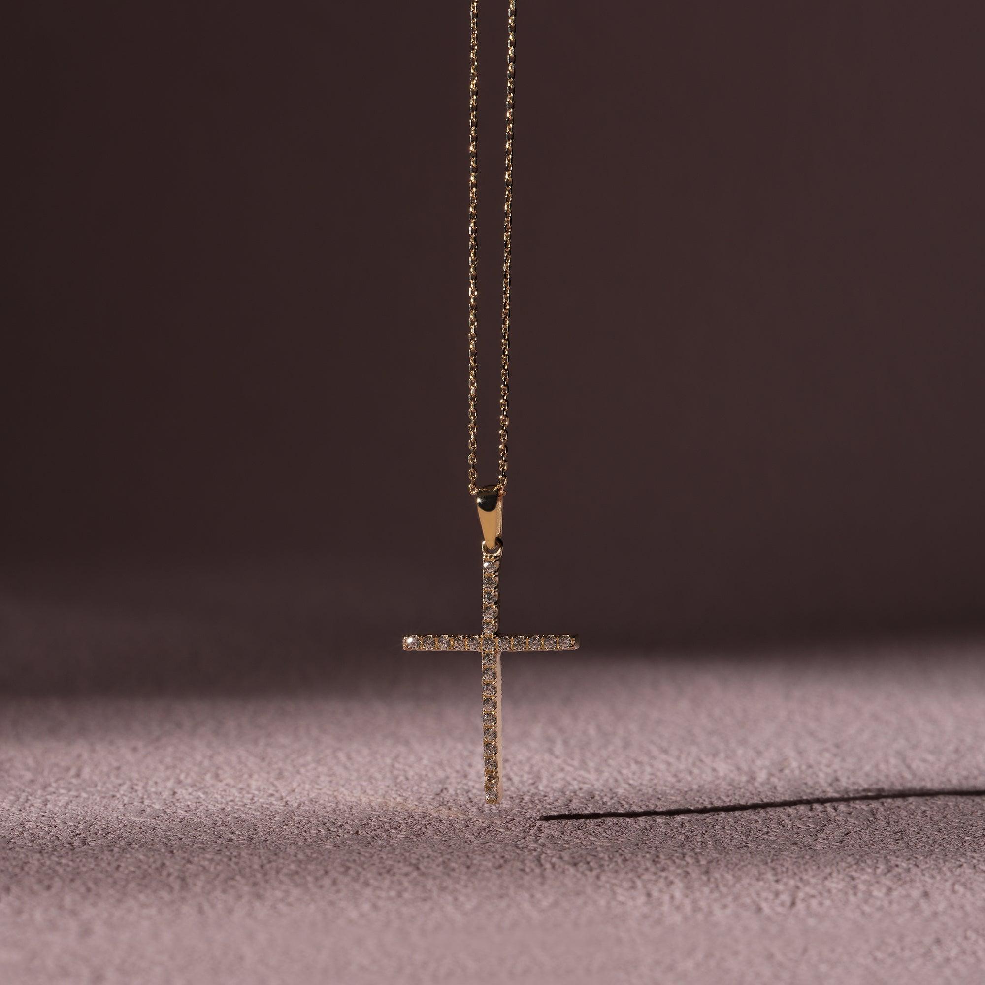 Gold cross pendant necklace with sparkling stones on a textured surface and dark background