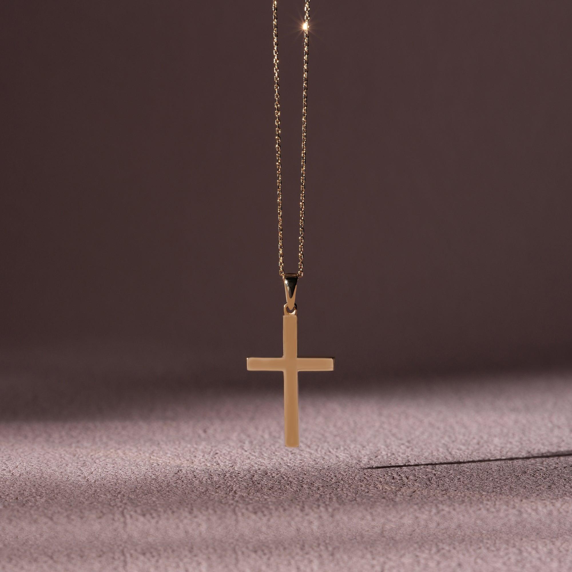 Gold cross pendant necklace on a delicate chain with a soft brown background