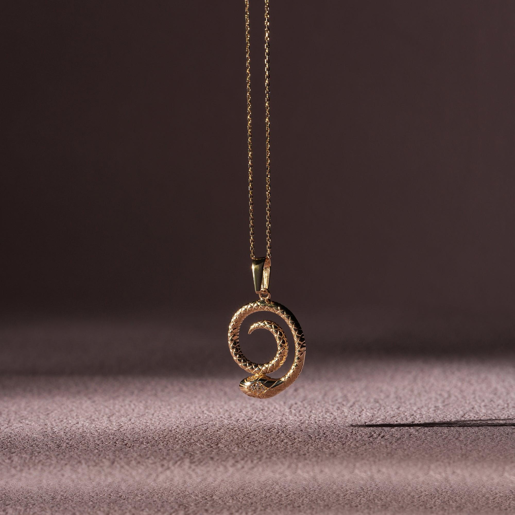 Gold snake pendant necklace with textured spiral design on a neutral background