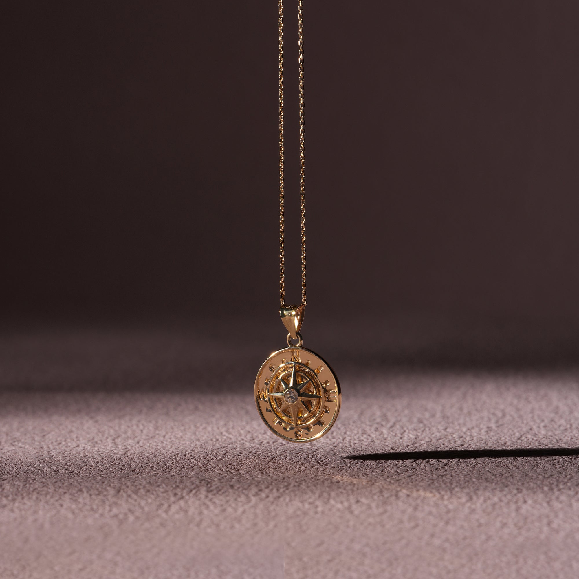 Gold compass pendant necklace on a textured surface with a dark background