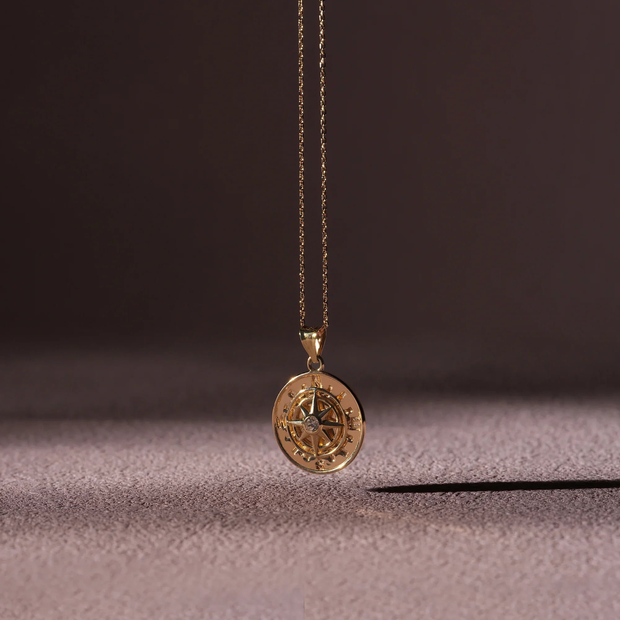 Gold compass pendant necklace on a textured surface with a dark background