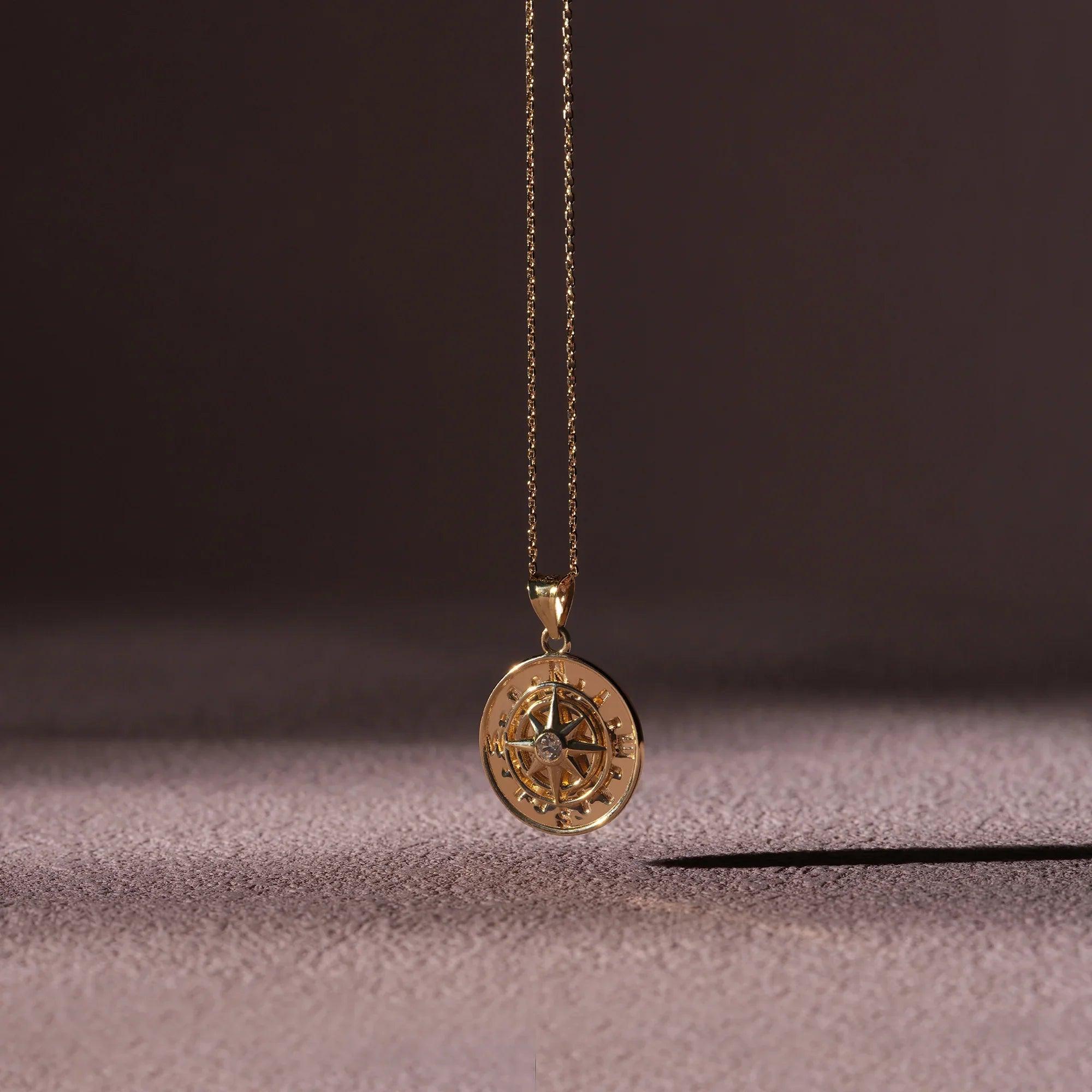 Gold compass pendant necklace with diamond accent on textured surface