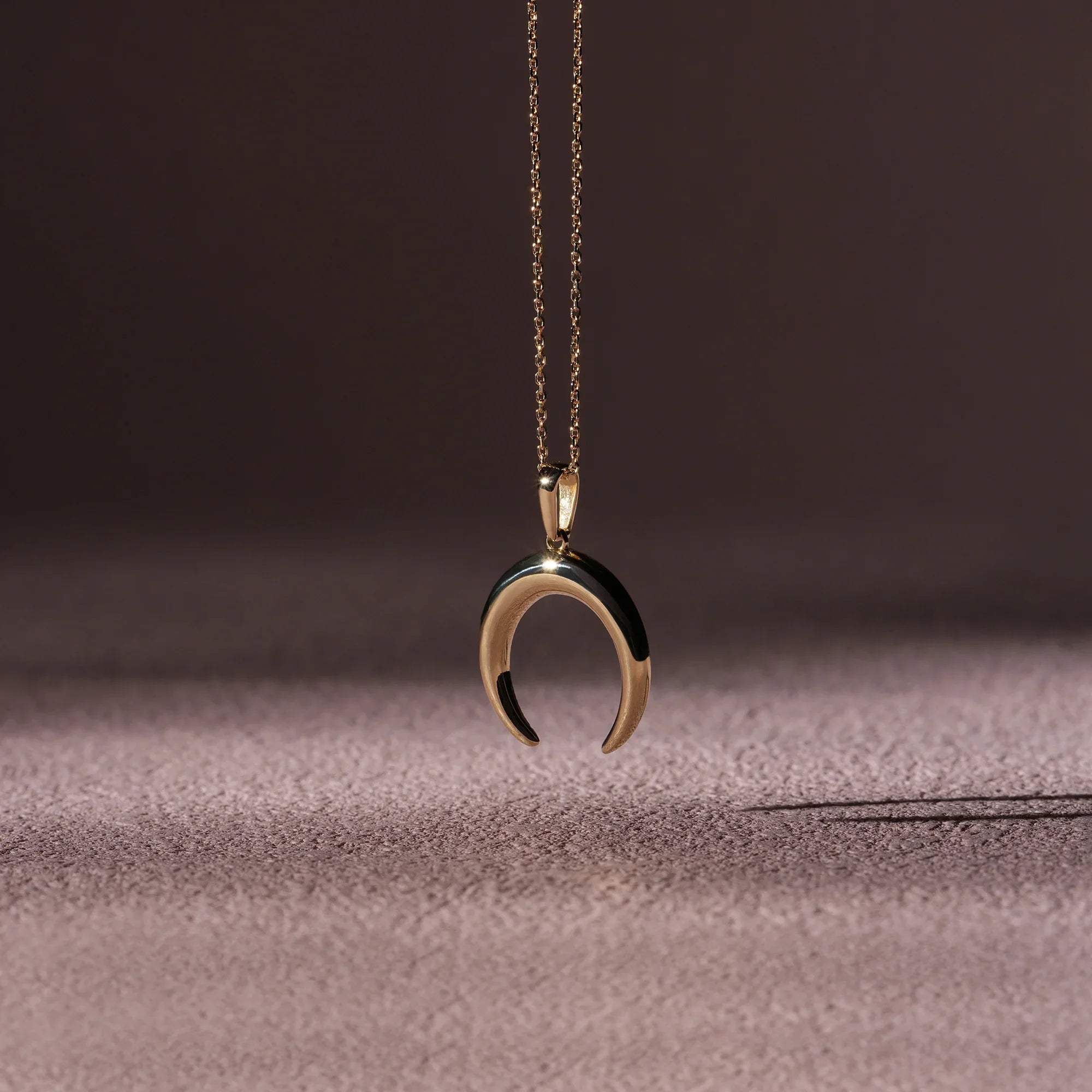 Gold crescent moon necklace on a textured surface with a dark background