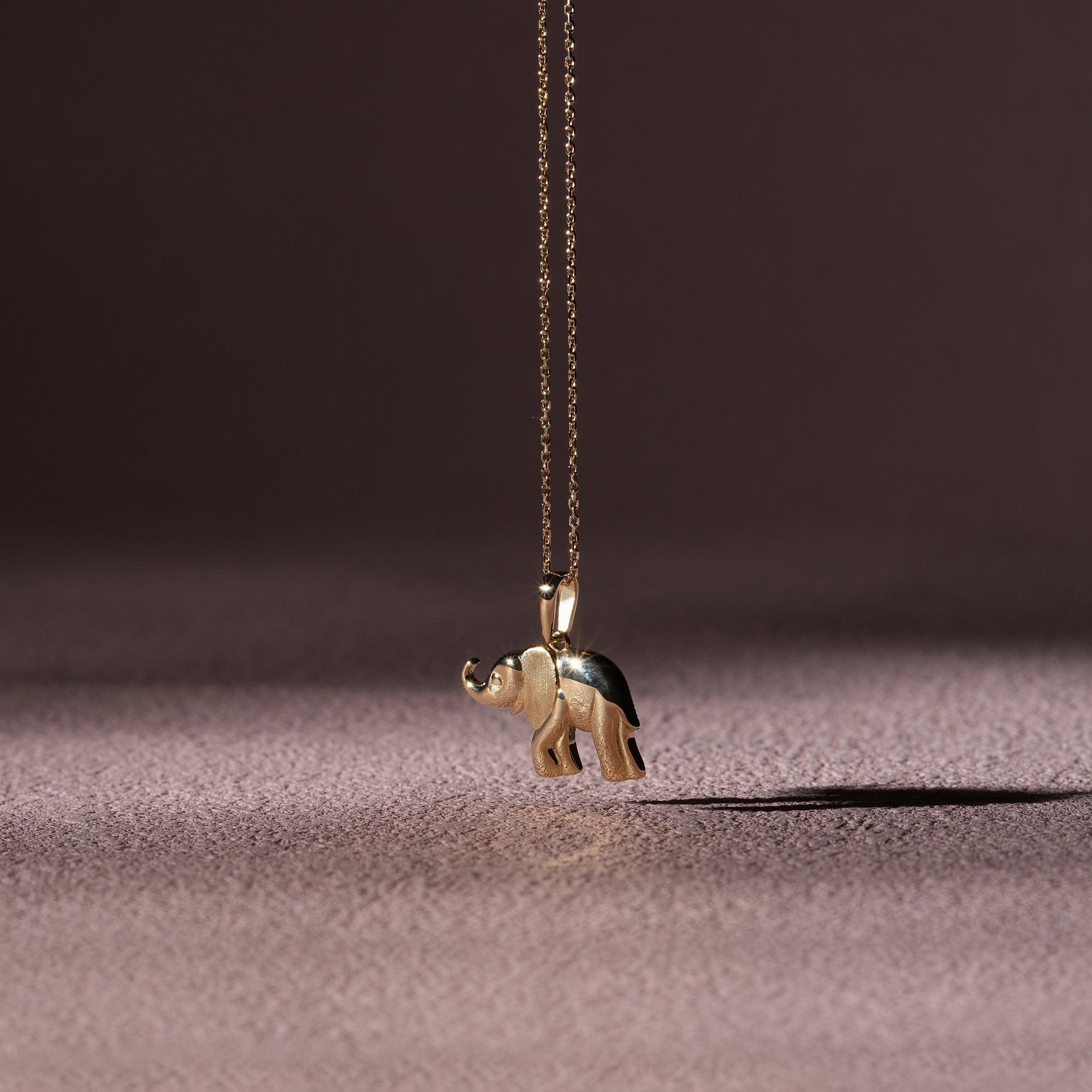 Gold elephant pendant necklace on a delicate chain with a soft textured background