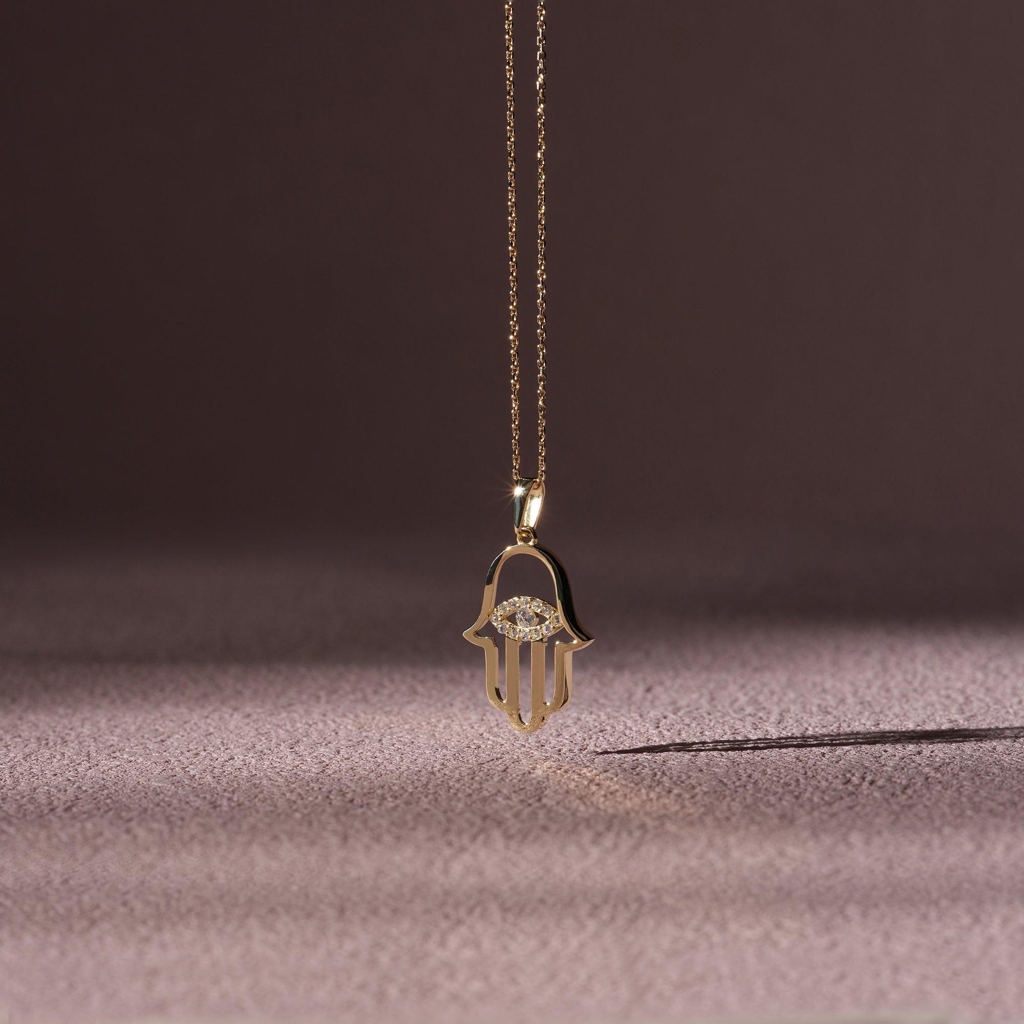 Gold Hamsa hand pendant necklace with diamonds on a soft textured background