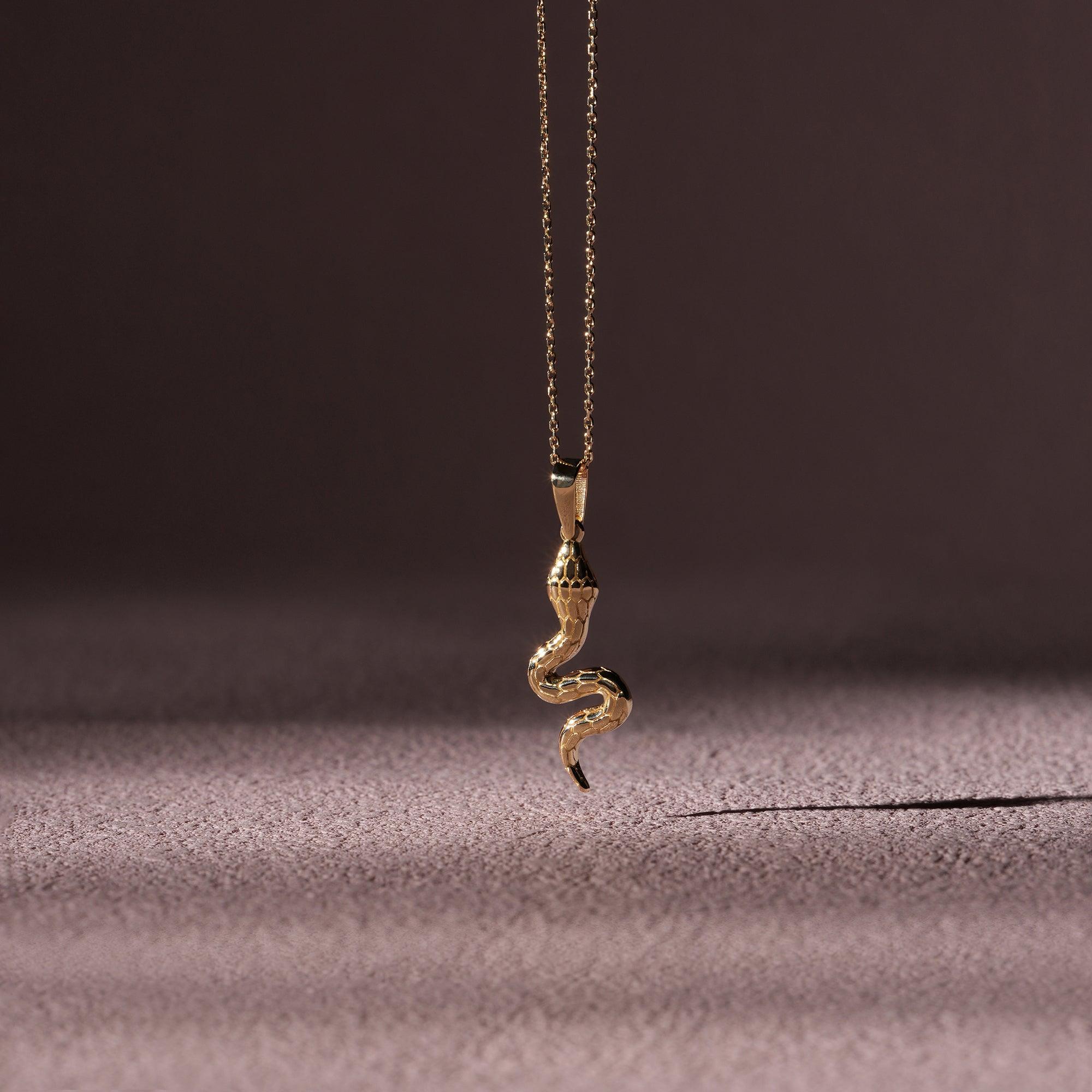 Gold snake pendant necklace with textured details on a soft purple background