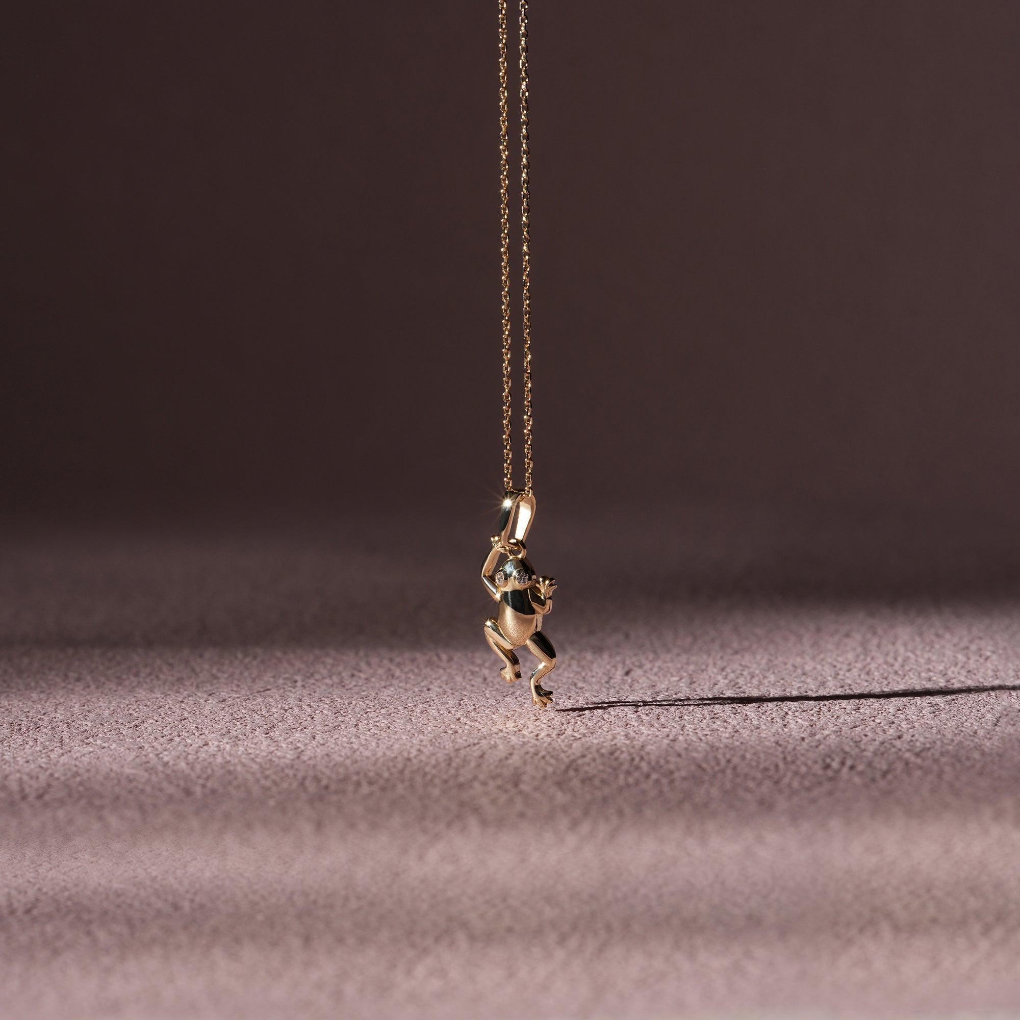 Gold frog pendant necklace on a dark fabric background