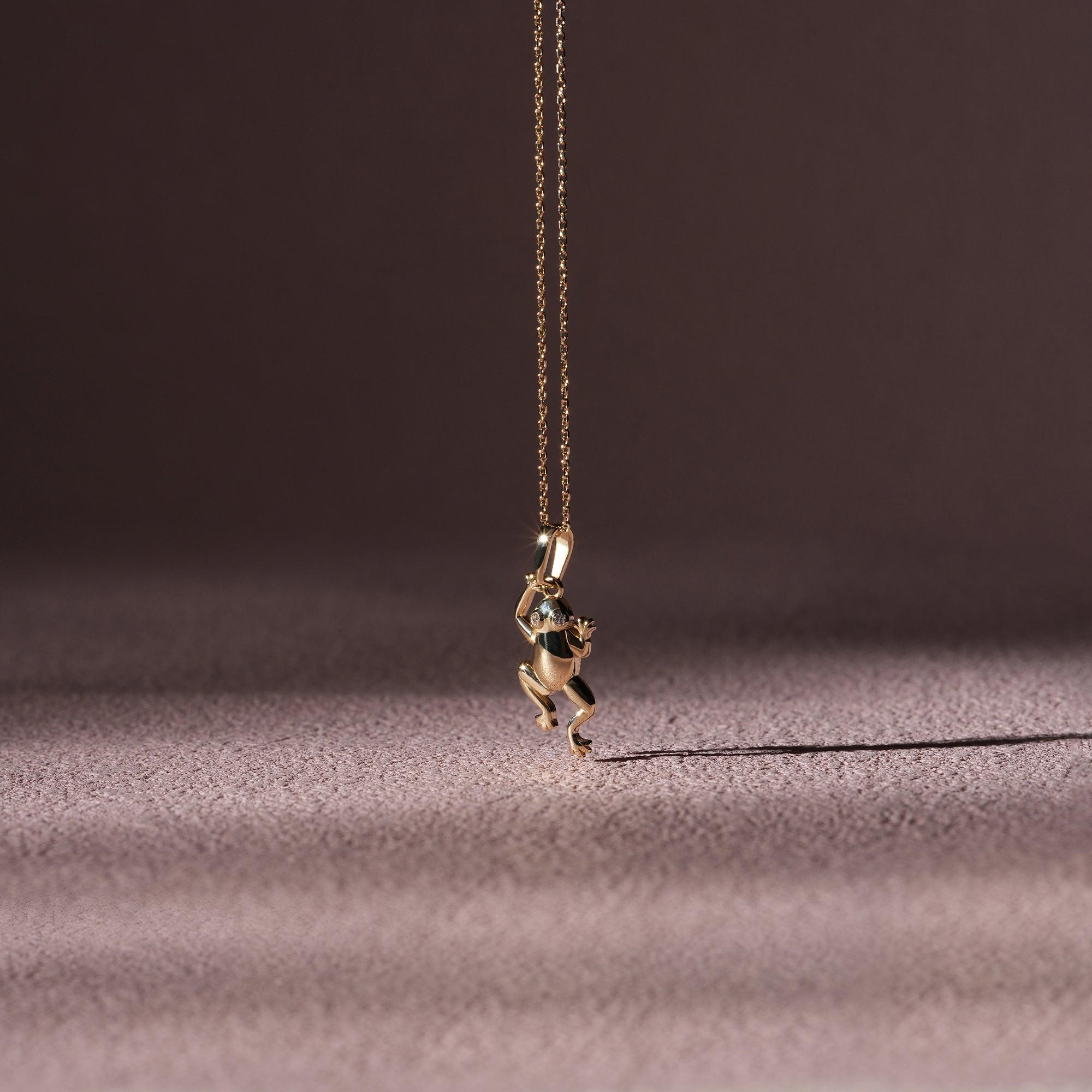 Gold frog pendant necklace with gemstone detail on a fine chain, elegant jewelry on soft background